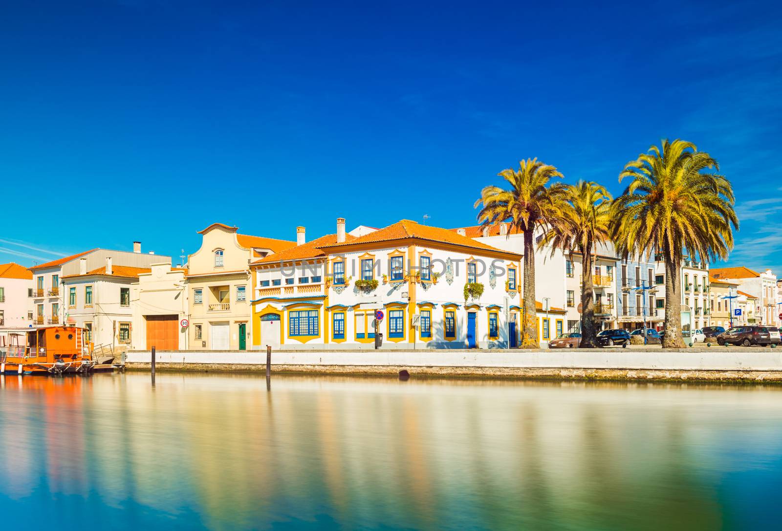 Cityscape of Aveiro, ("The Portuguese Venice"), Portugal. View of embankment with colorful buildings in the traditional architecture style, canal for boats and ships and several big palm trees
