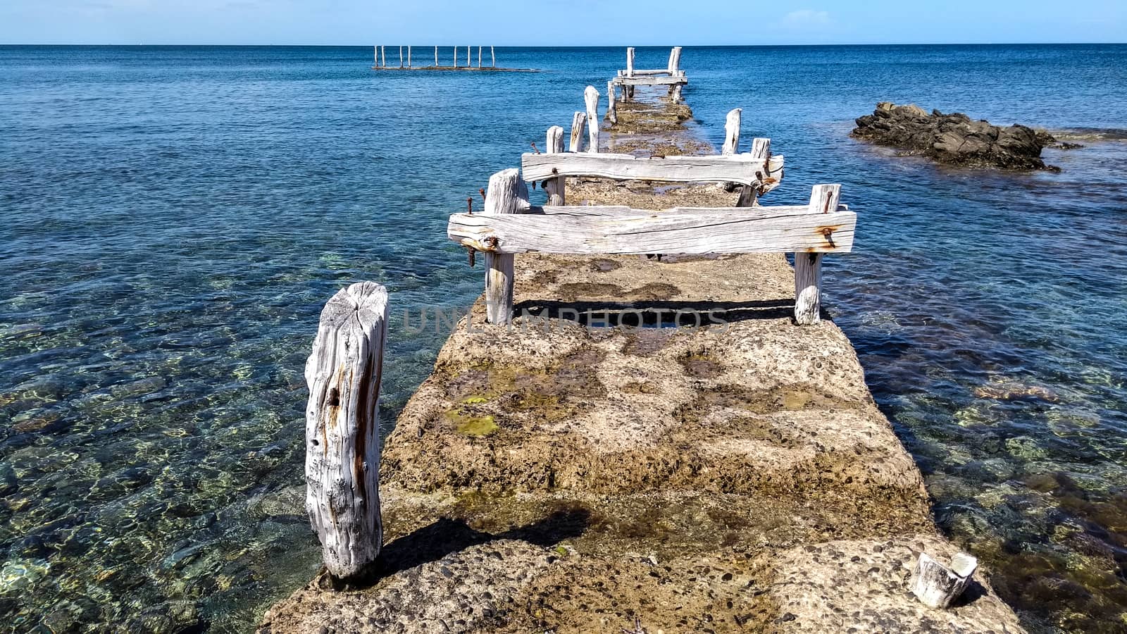 Ancient disused pier with wooden structures corroded by the atmospheric events that made it white on the crystal clear blue sea by robbyfontanesi