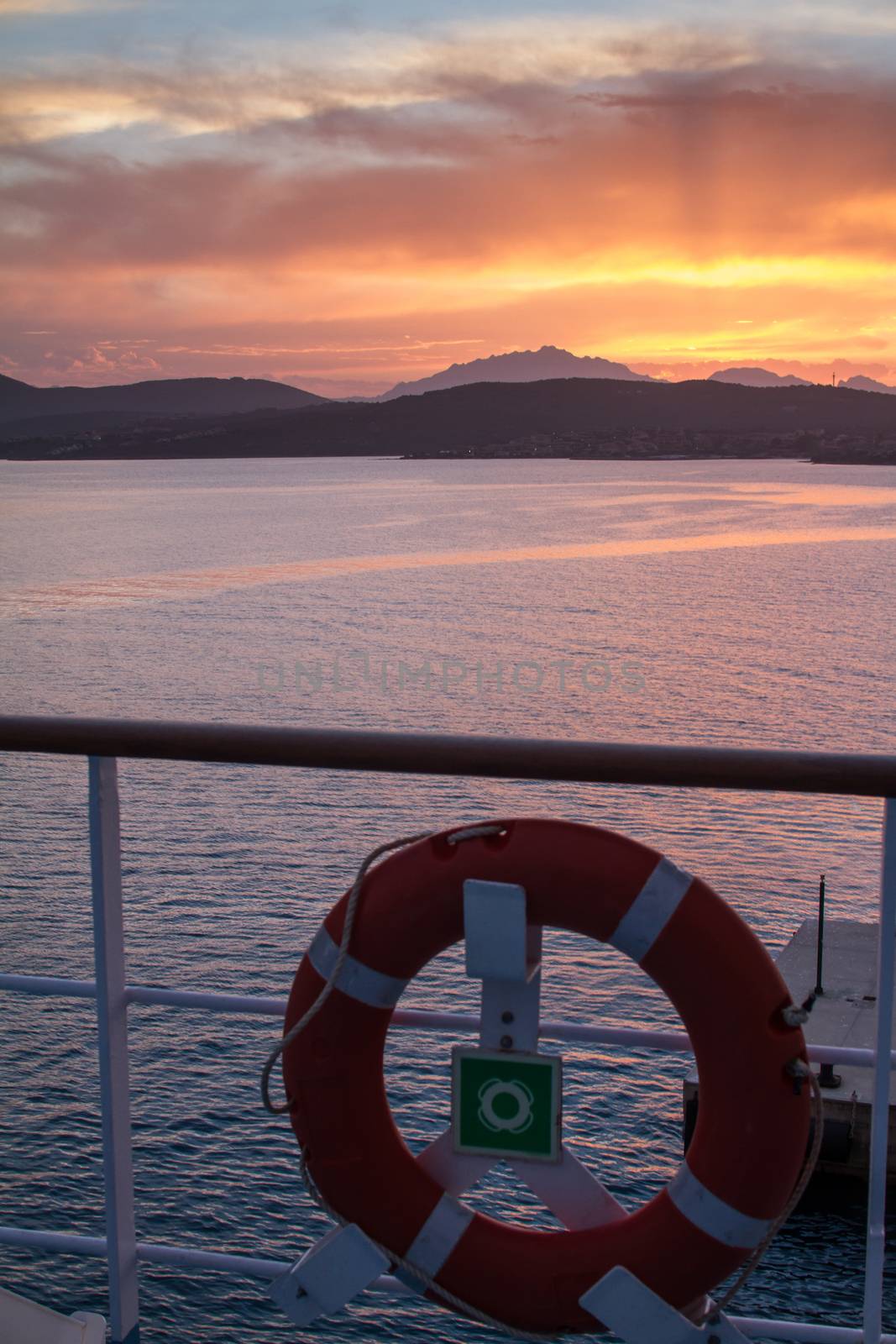 Sunrise on the Sardinian sea coast with intense orange color seen from the sea on the ferry that is about to dock with lifebuoy in the foreground