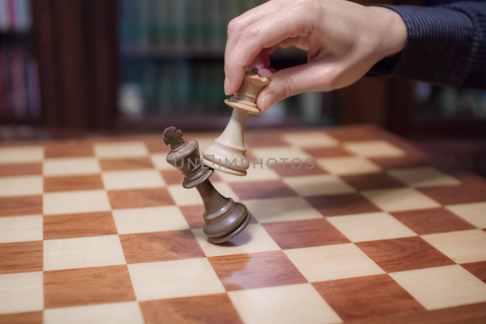 Concept: the woman who dominates the man. A woman's hand gives checkmate to the king with the queen on a wooden chessboard, with no other pieces in play