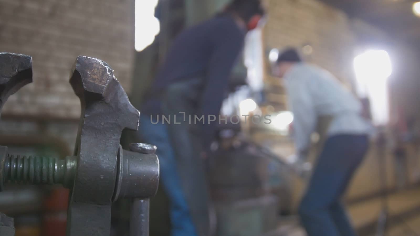 Blacksmith forging red hot iron on anvil - automatic hammering, de-focused shot