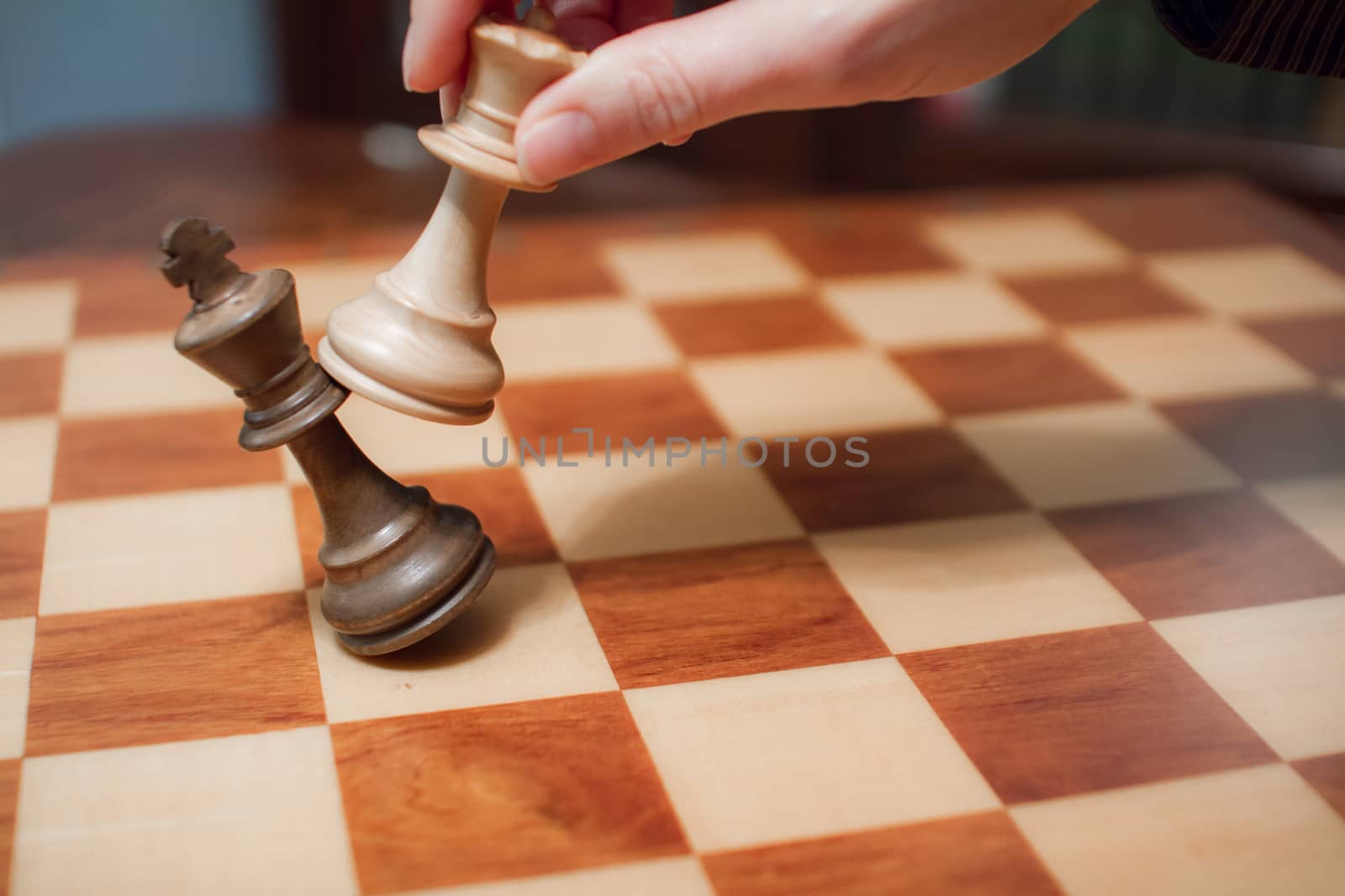 Concept: the woman who dominates the man. A woman's hand gives checkmate to the king with the queen on a wooden chessboard, with no other pieces in play