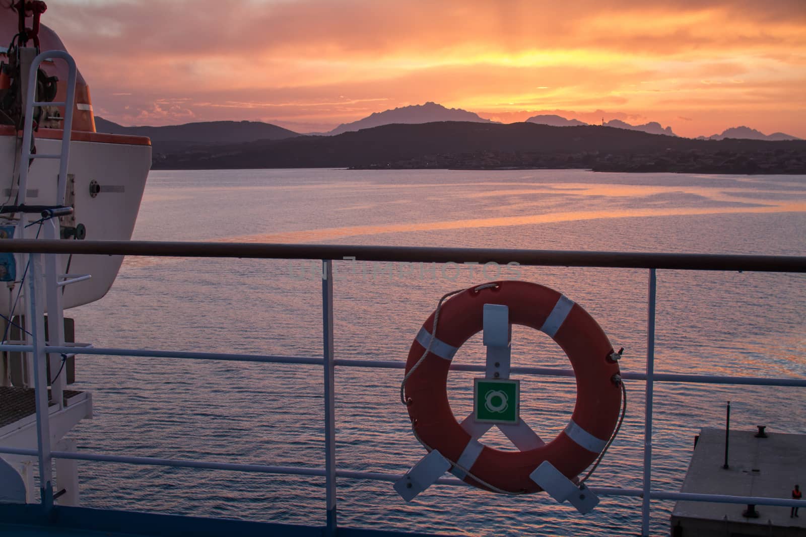 Sunrise on the Sardinian sea coast with intense orange color seen from the sea on the ferry that is about to dock with lifebuoy in the foreground