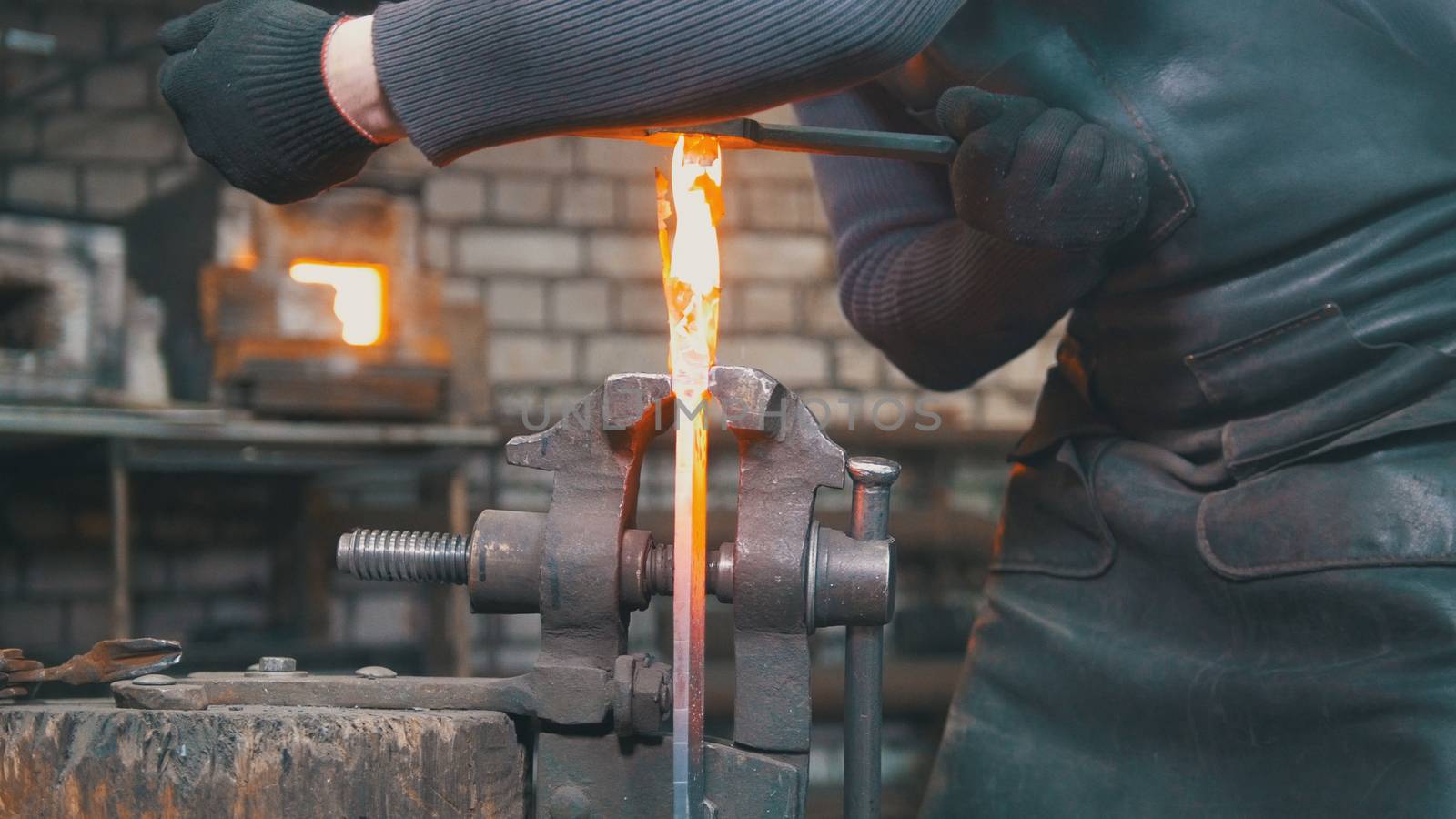 Muscular blacksmith in forge hammering steel products, small business
