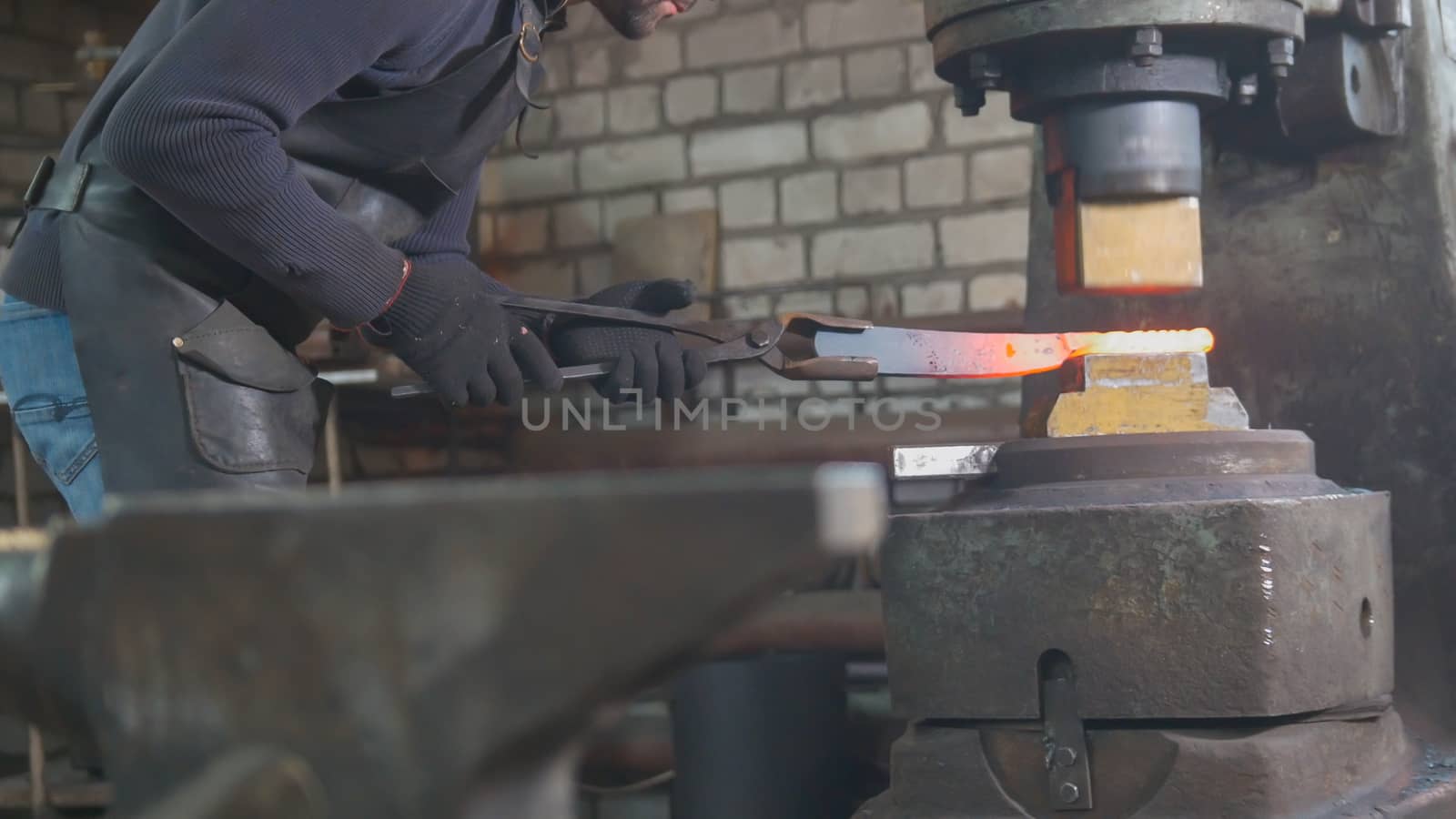 Man blacksmith forges the metal at the mechanical hammer - small business,
