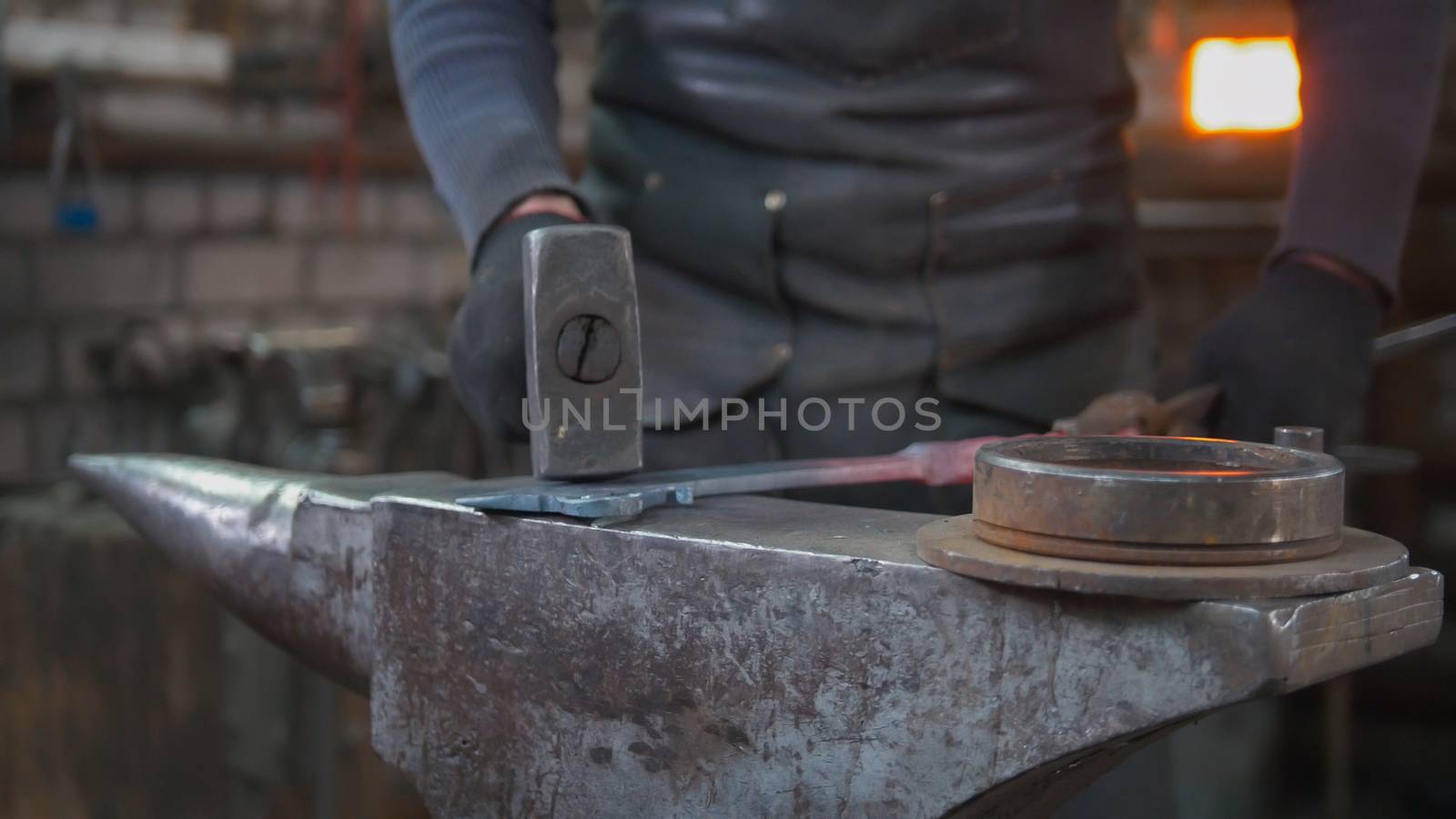 Muscular man blacksmith with hammer in forge creating steel knife by Studia72