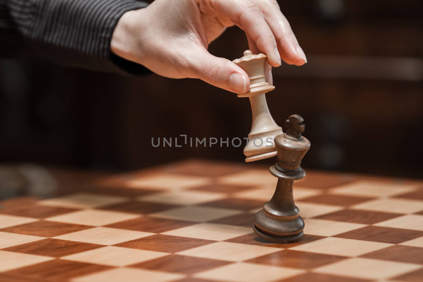 Concept: the woman who dominates the man. A woman's hand gives checkmate to the king with the queen on a wooden chessboard, with no other pieces in play