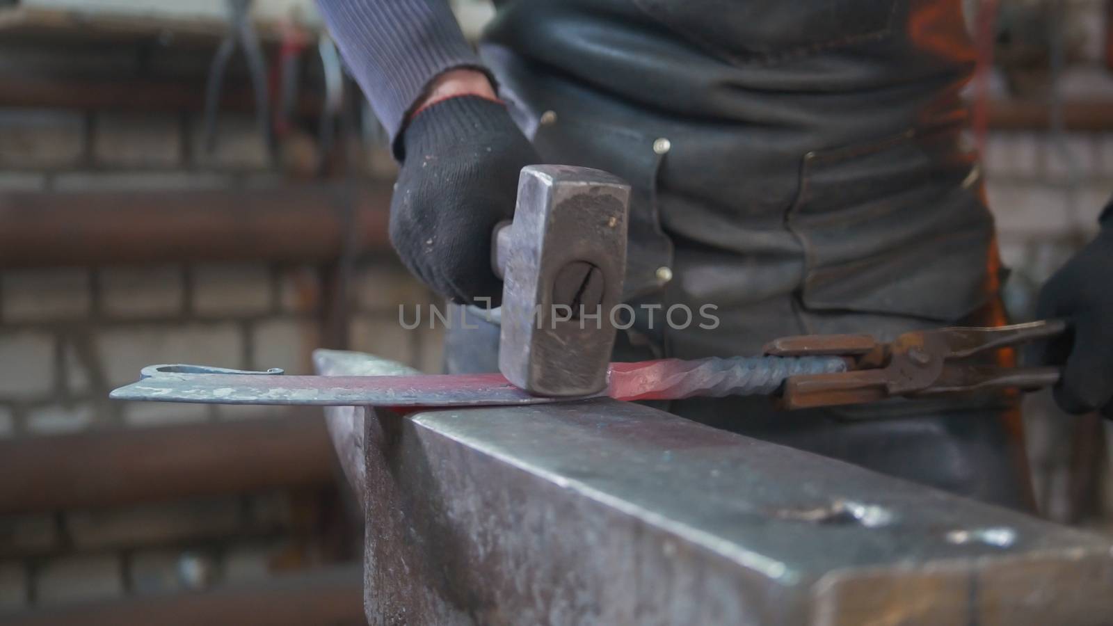 Muscular man blacksmith with hammer in forge creating steel knife, small business