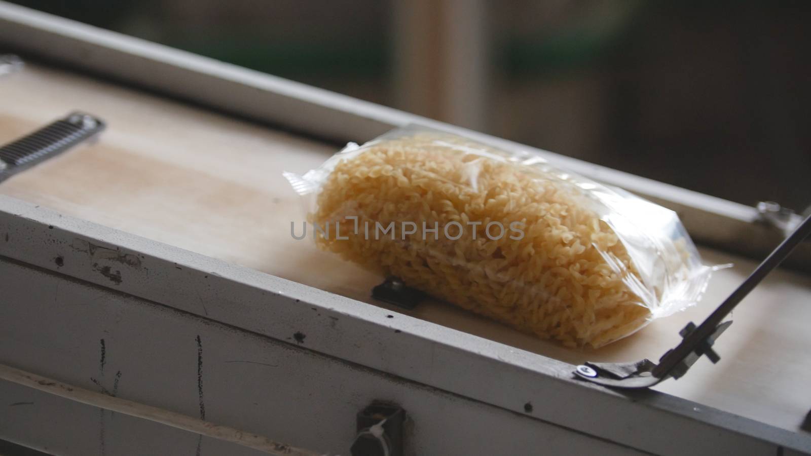 Food factory - conveyor with plastic pack of macaroni, close up