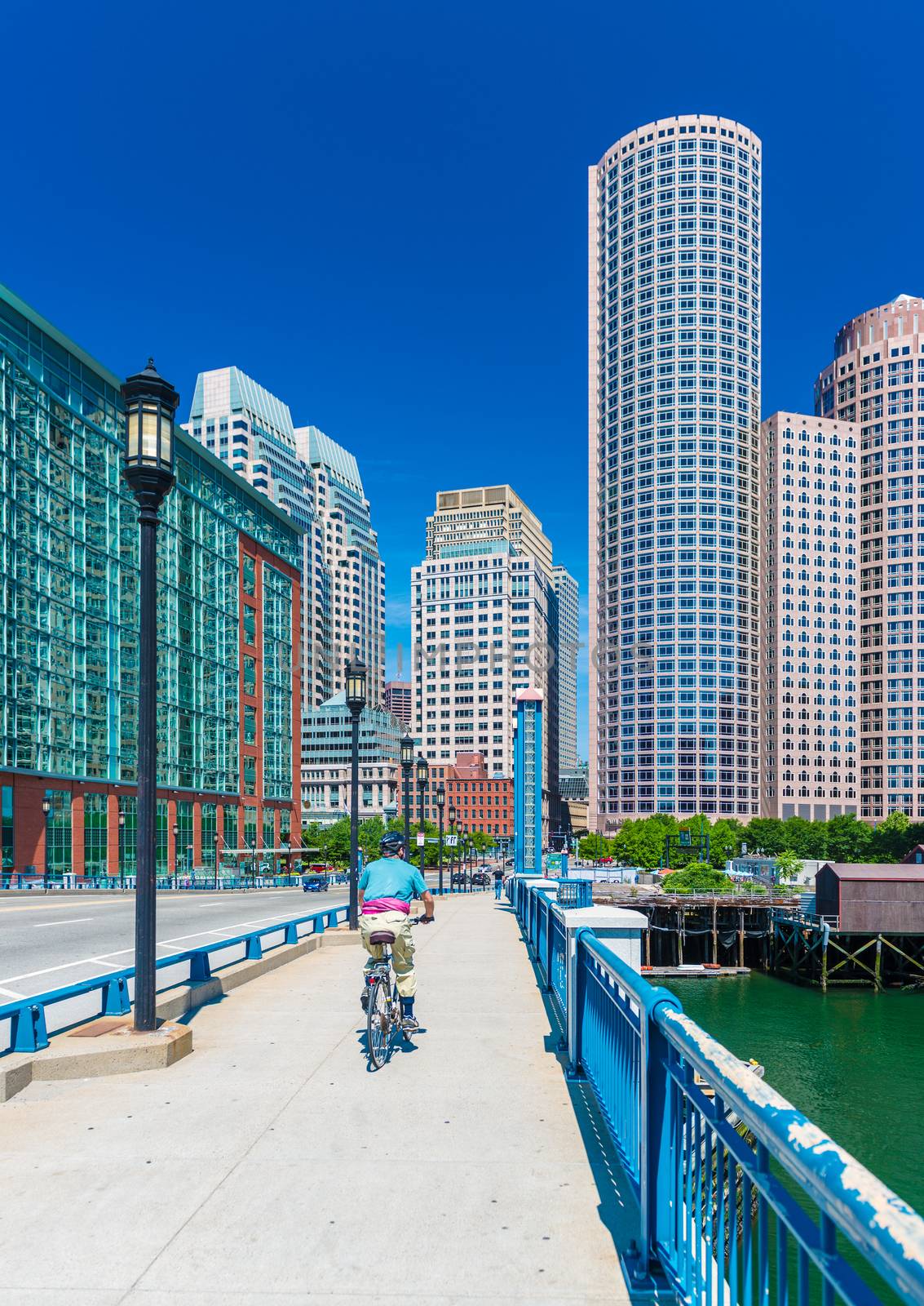 Boston, MA - June 2016, USA: Man cycling on bridge towards Boston downtown in sunny summer day