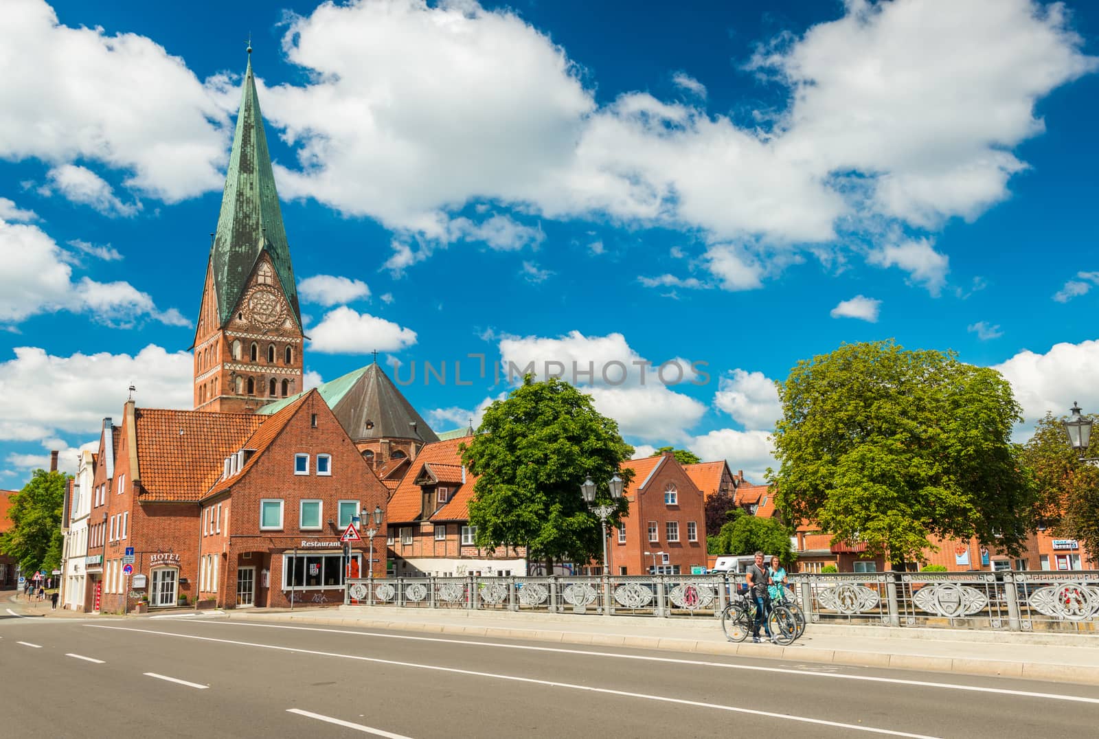 Luneburg - July 2018, Lower Saxony, Germany: People walking along the bridge. Cathedral and old historical houses with blue sky and clouds on the background
