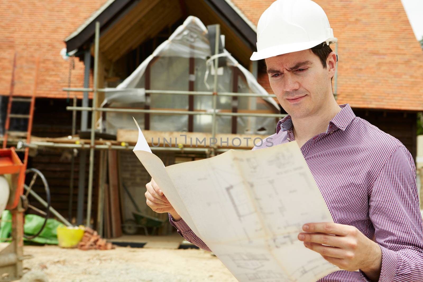Architect On Building Site Looking At House Plans by HWS