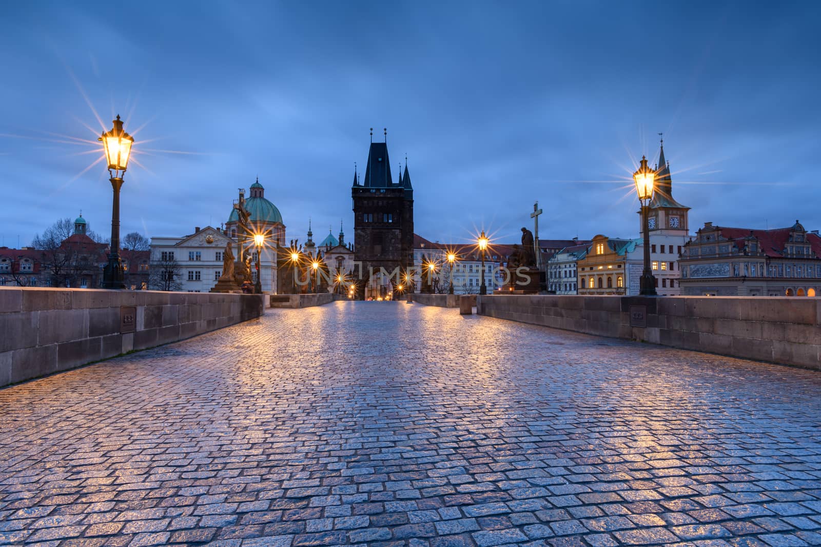 Historic bridge in Prague at sunrise with lights reflecting on the wet stone