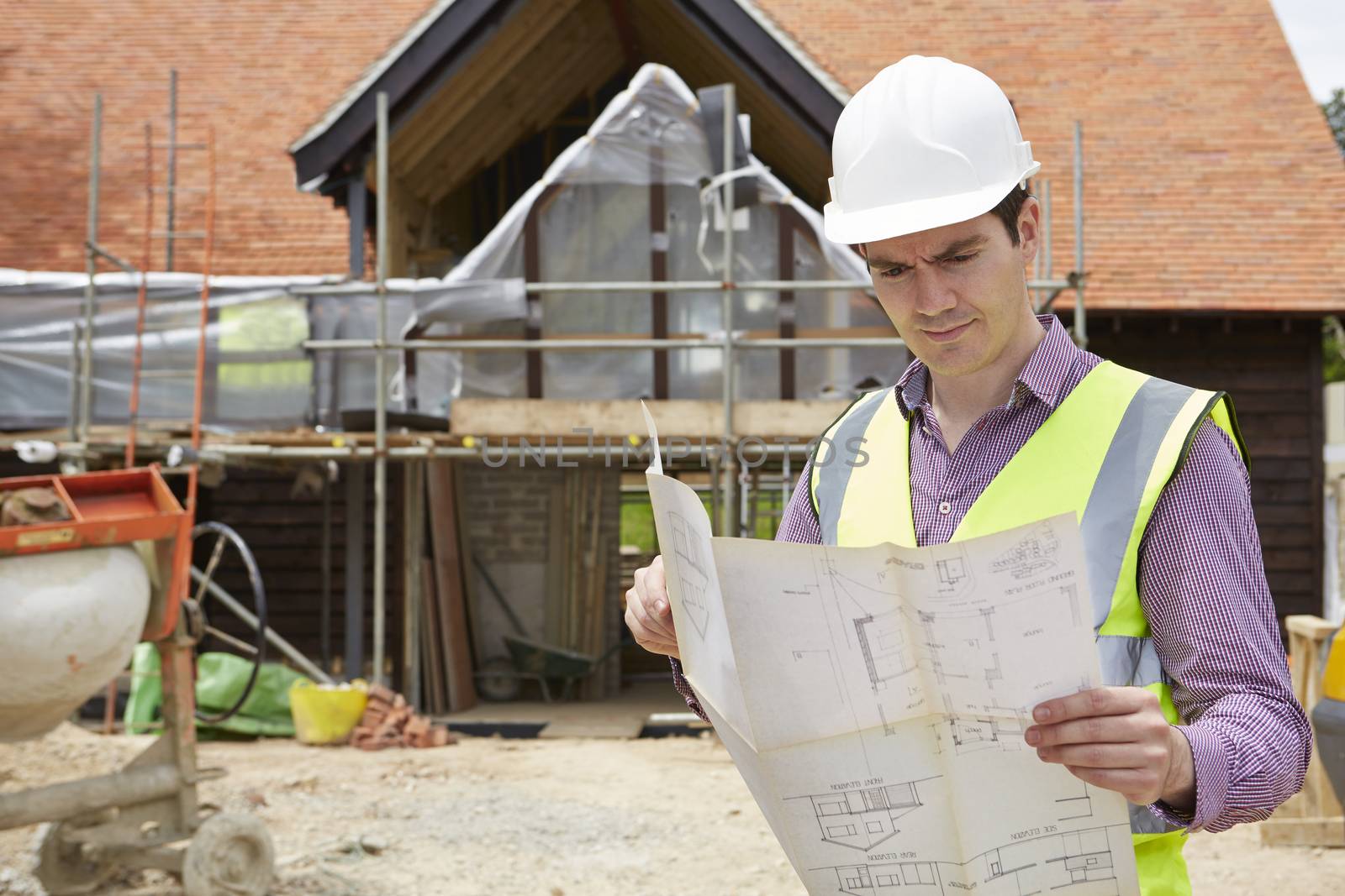 Architect On Building Site Looking At House Plans by HWS