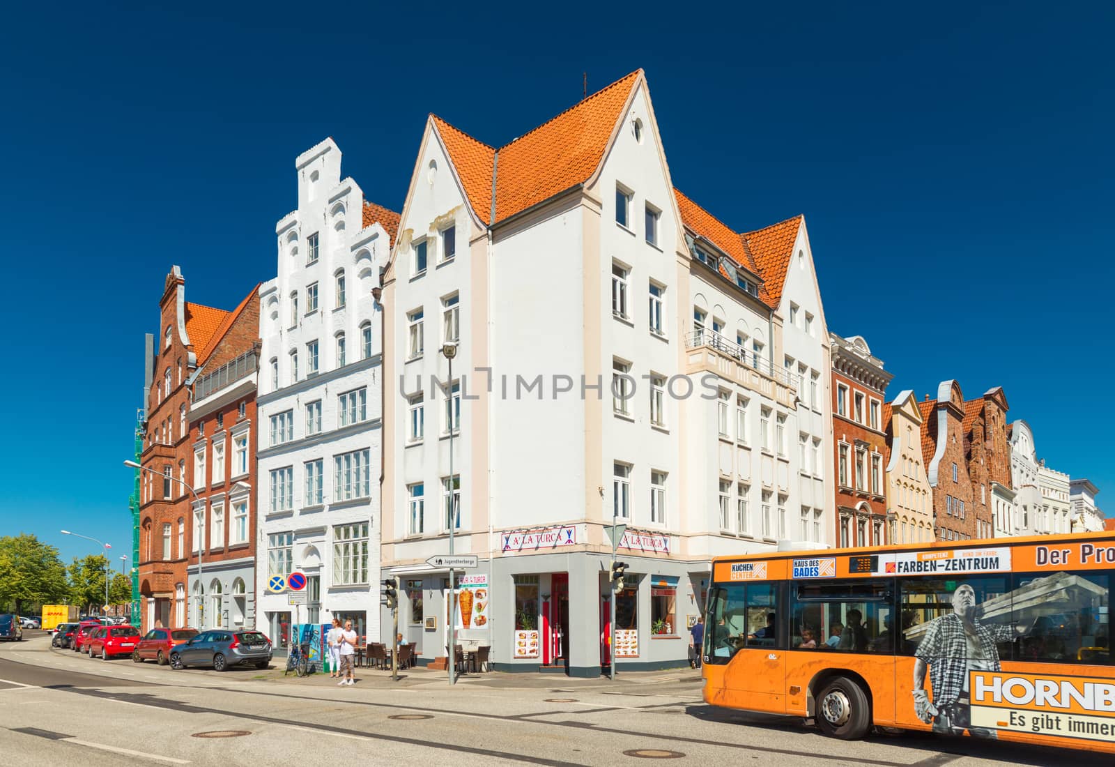 Lubeck - July 2018, Germany: Historical buildings near the embankment of Lubeck. Traditional architecture style, white and red brick houses with orange roofs. Bus is driving along the street