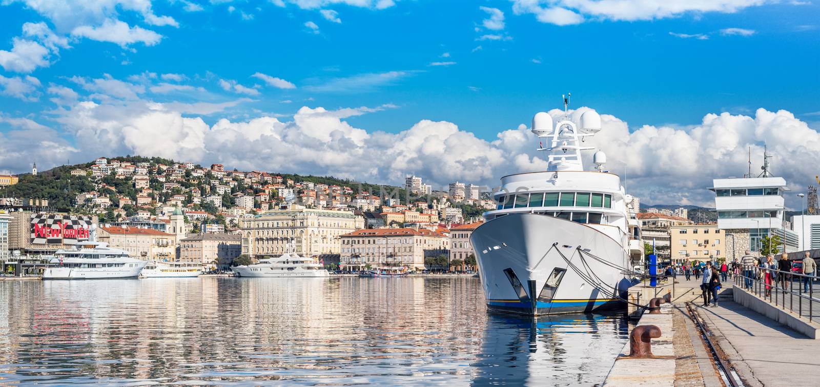 Rijeka - June of 2012, Croatia: View of Rijeka harbor, white ship at the pier, people are walking along promenade, cityscape in sunny day with blue sky and clouds