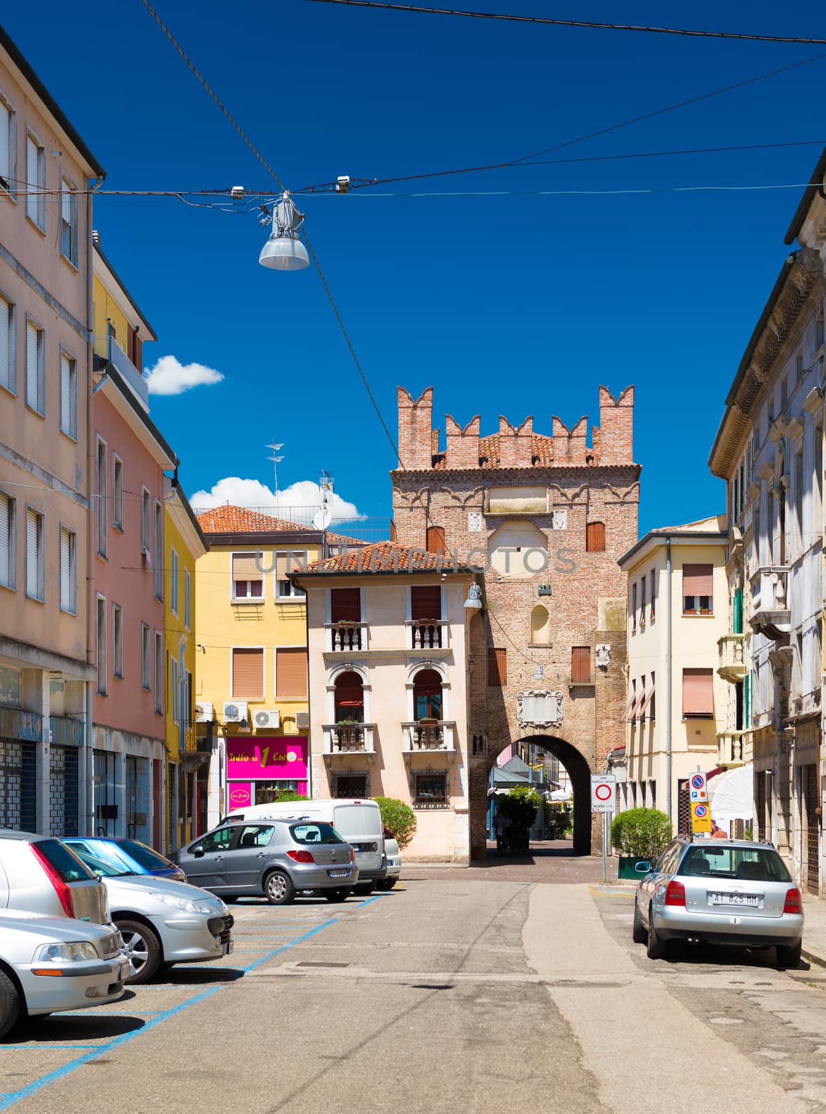 Rovigo - July 2017, Veneto region, Italy: View of the old tower with arch, surrounding buildings and parked cars