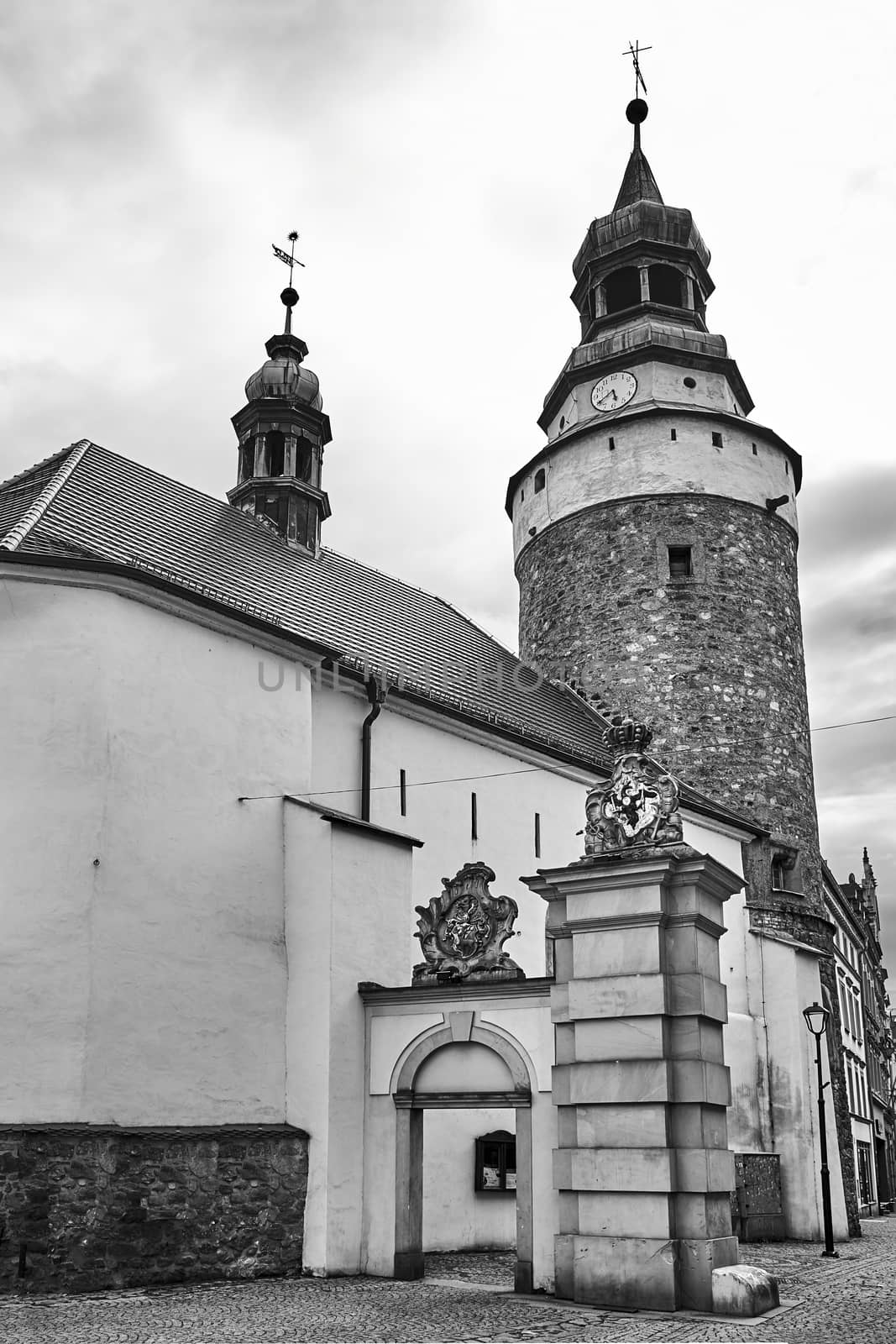 A medieval, stone church with a bell tower and a fragment of the city gate in Jelenia Gora in Poland, black and white