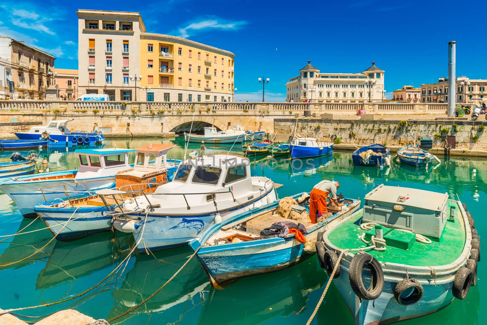 Syracuse - April 2019, Sicily, Italy: Cityscape of Syracuse with colorful boats, bridge and historical buildings with blue sky in the background