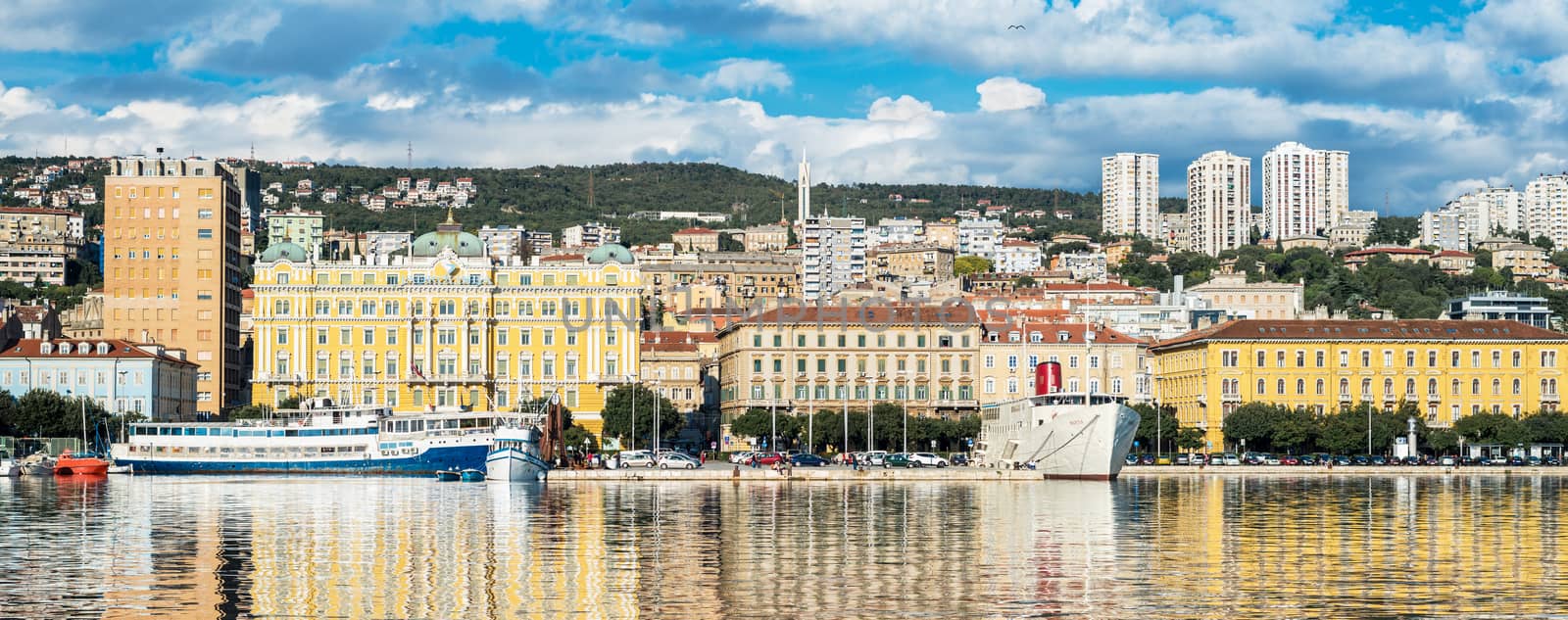 Rijeka - June of 2012, Croatia: Rijeka cityscape reflected in the water, Jadrolinija building and ships in harbour, old and modern buildings against the green hills and cloudy sky