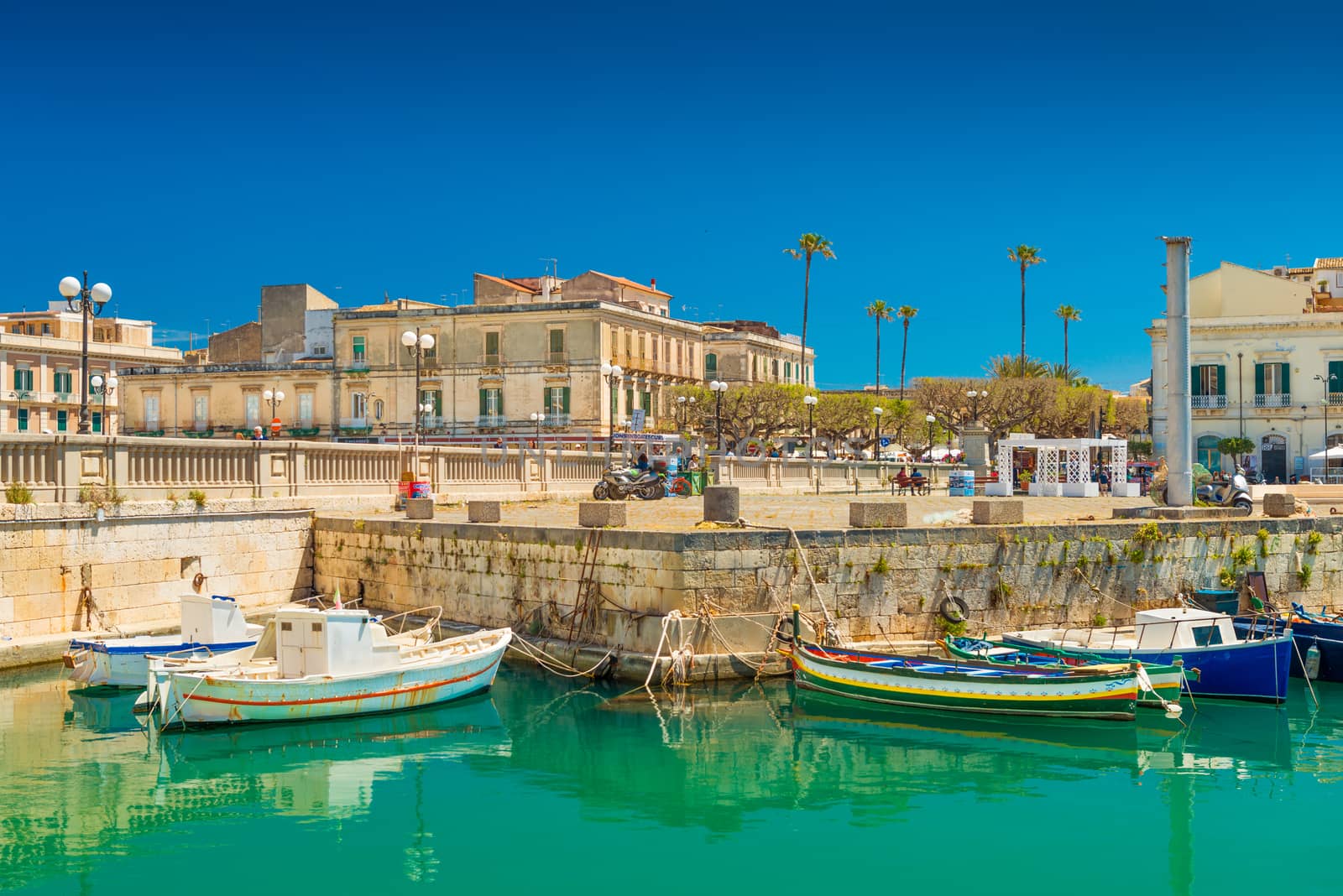 Syracuse - April 2019, Italy: Cityscape of Syracuse and a small Island Ortygia, historical part of the city. Colorful boats lying on water near a stone pier