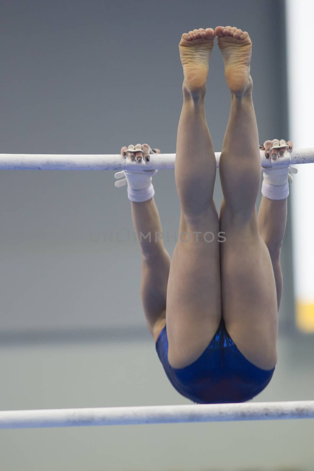 Athletic woman gymnasts performing on the bar at the championship by Studia72