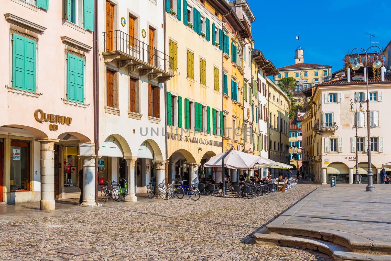 Udine - February 2017, Friuli Venezia Giulia, Italy: The street of Udine with traditional architecture and the stone pavement. Central square of the city. People sitting in cafe