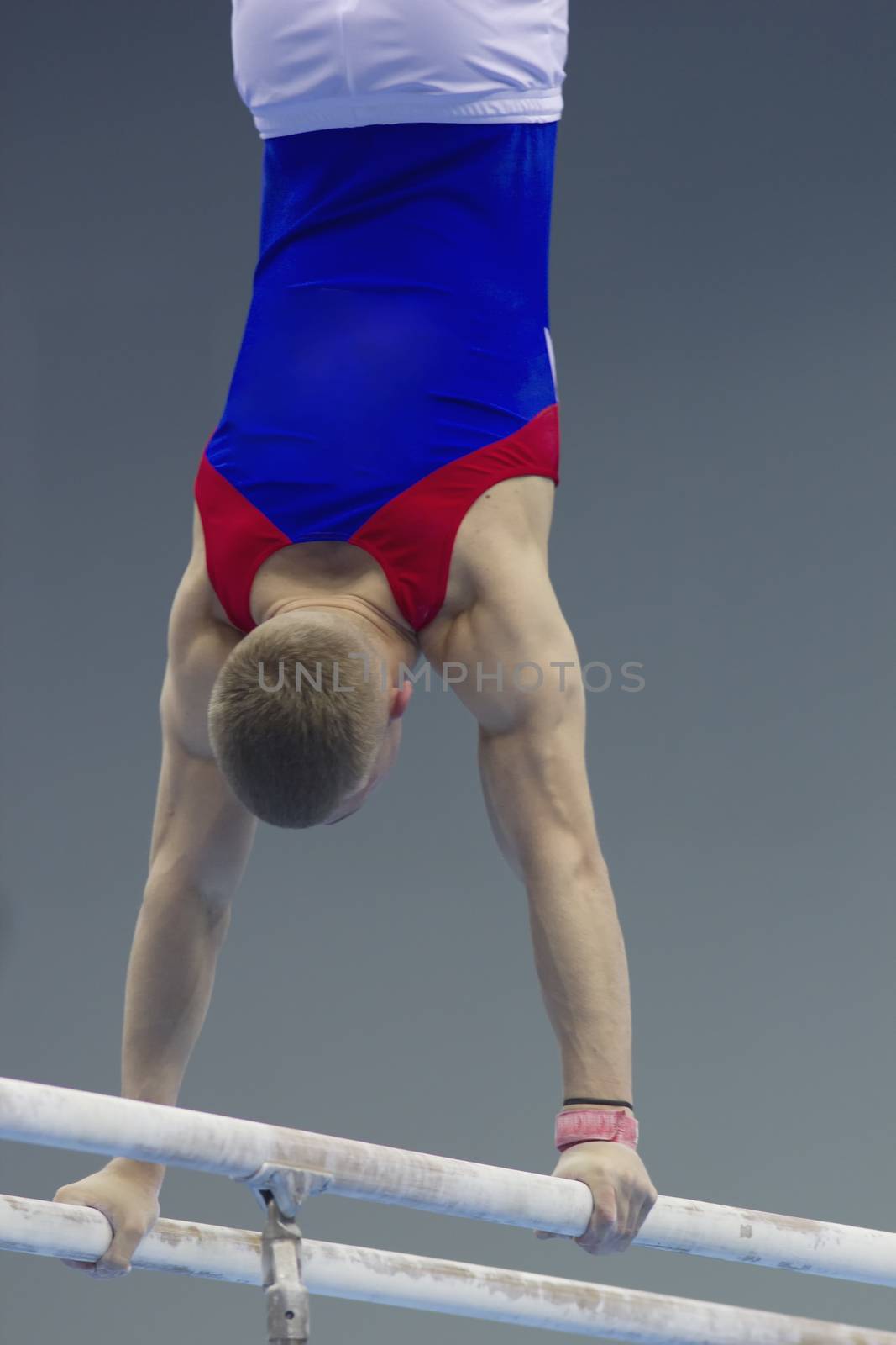 Rear view of muscular man gymnasts competing on the bar by Studia72