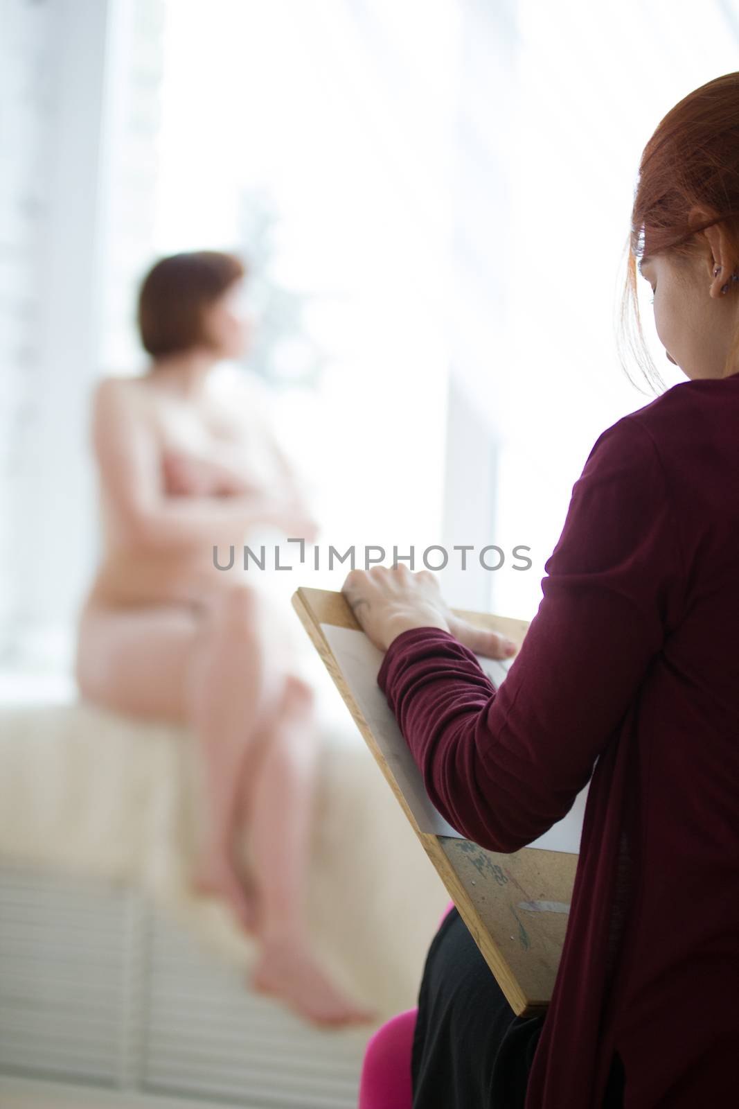 Rear view of female painter drawing on the wooden tablet nude woman, close up