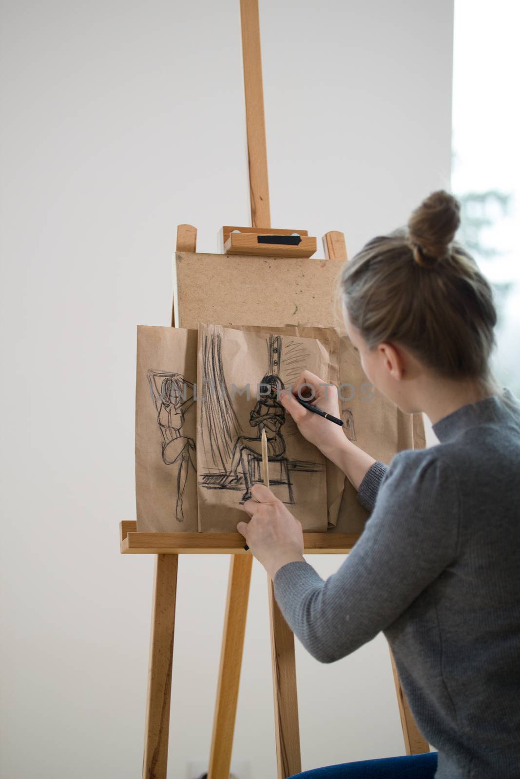 Rear view of female painter draws on the easel human figure, telephoto shot
