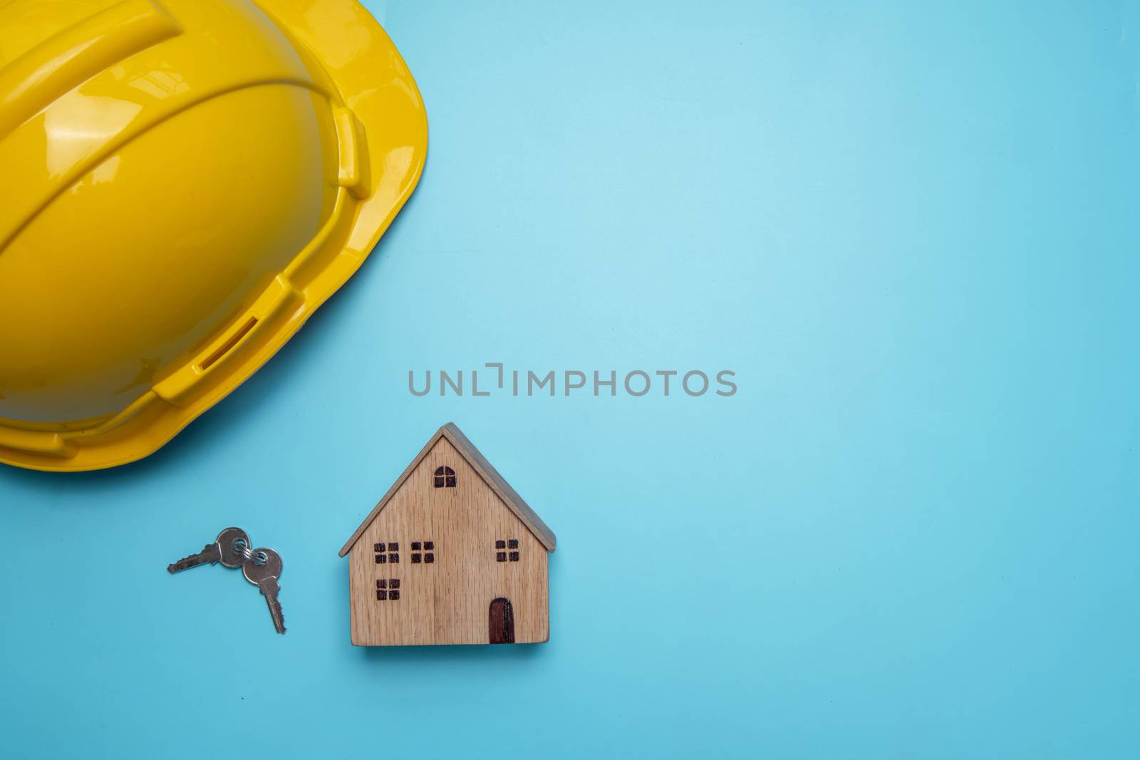 helmet with wooden house and key on blue background, real estate concept