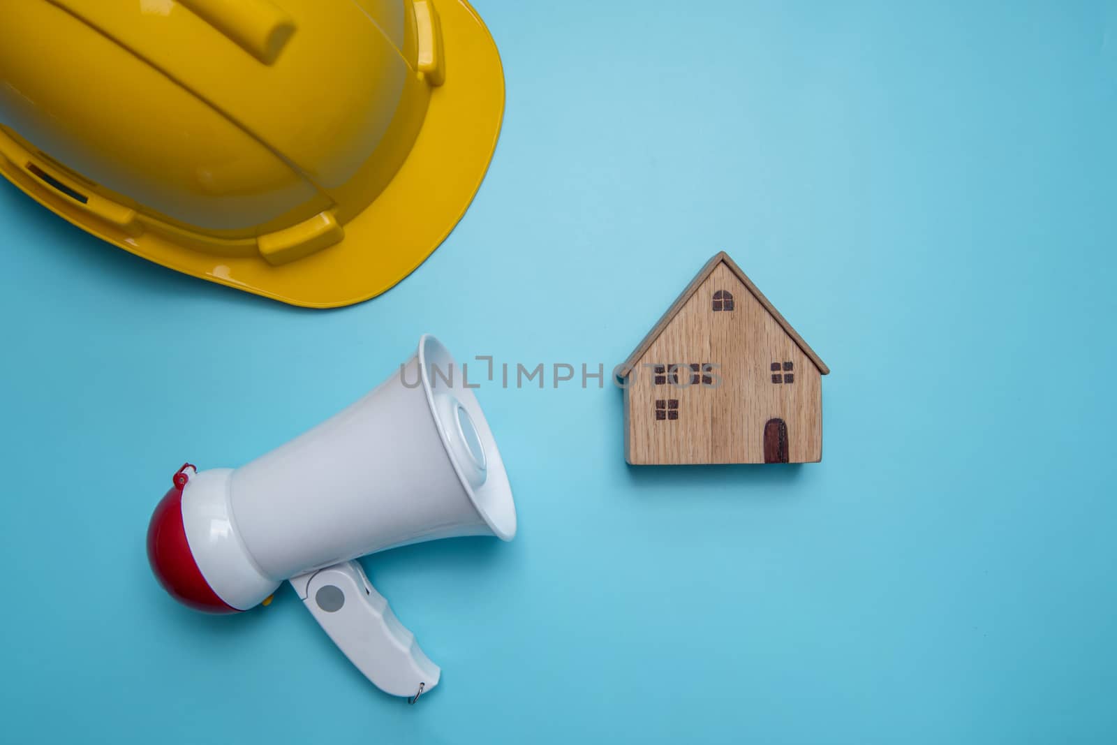 Announcement and announce advertising background public relations about construction building, home, house and real estate with megaphone and yellow helmet on blue background 