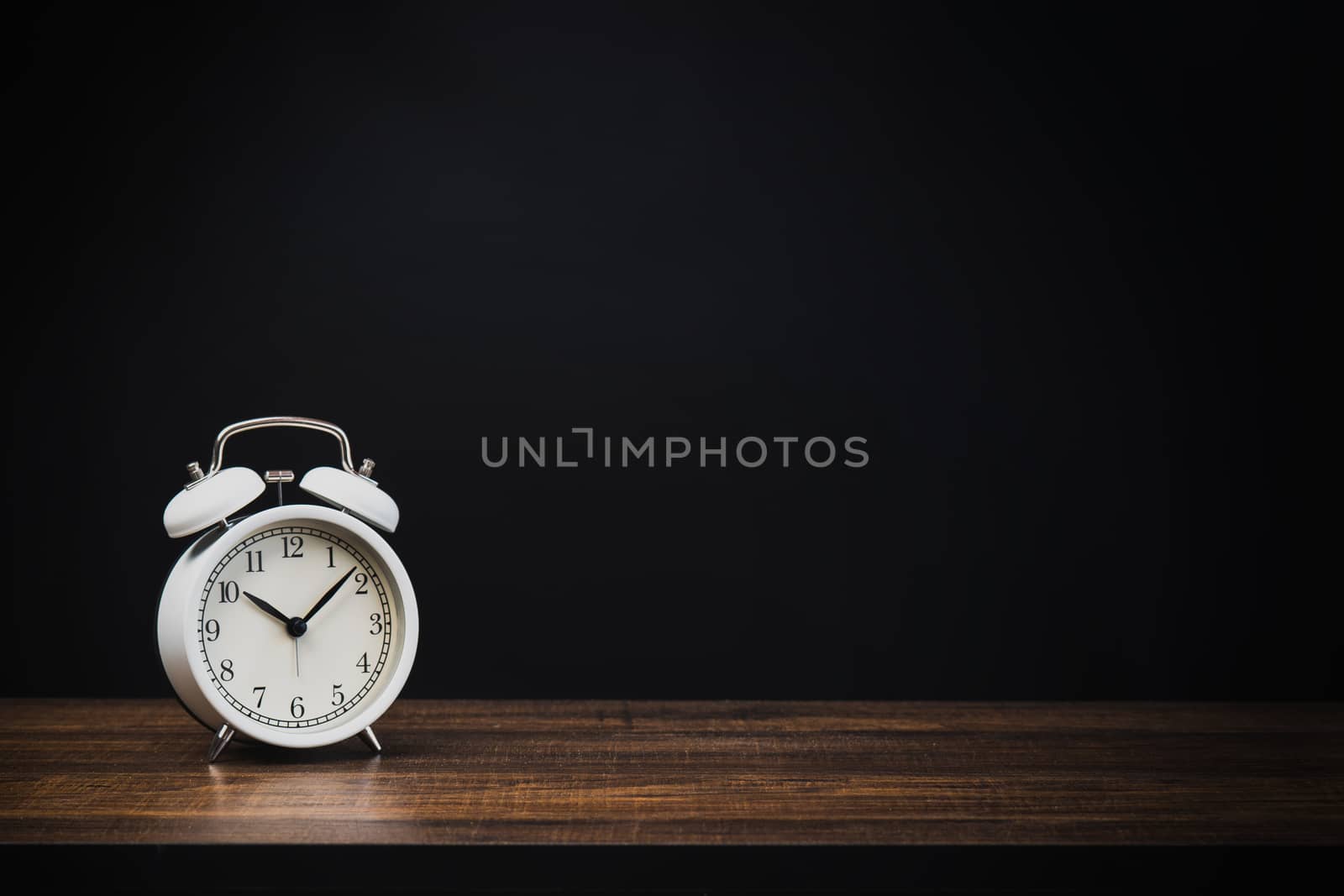 white alarm clock on wood table at night with dark or black background 