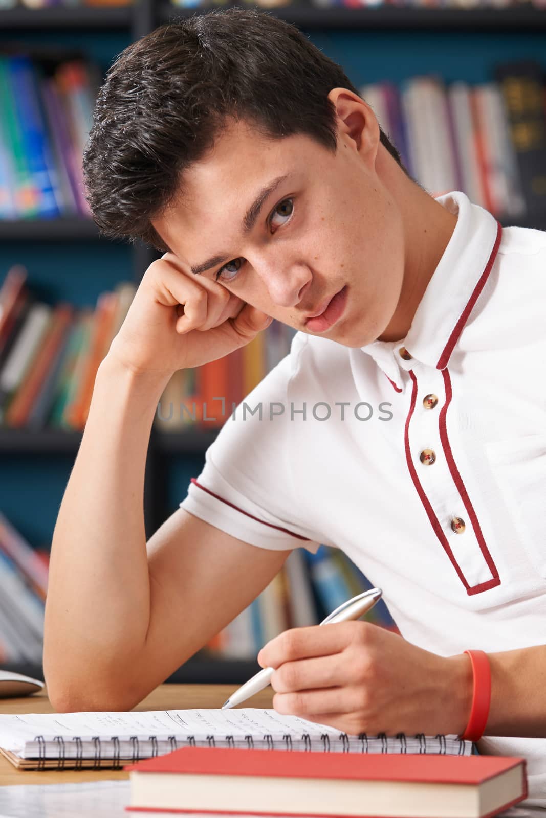 Fed Up Male Teenage Student Working In Library