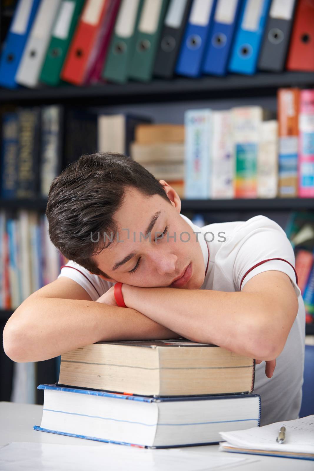 Tired Male Teenage Student Sleeping In Library