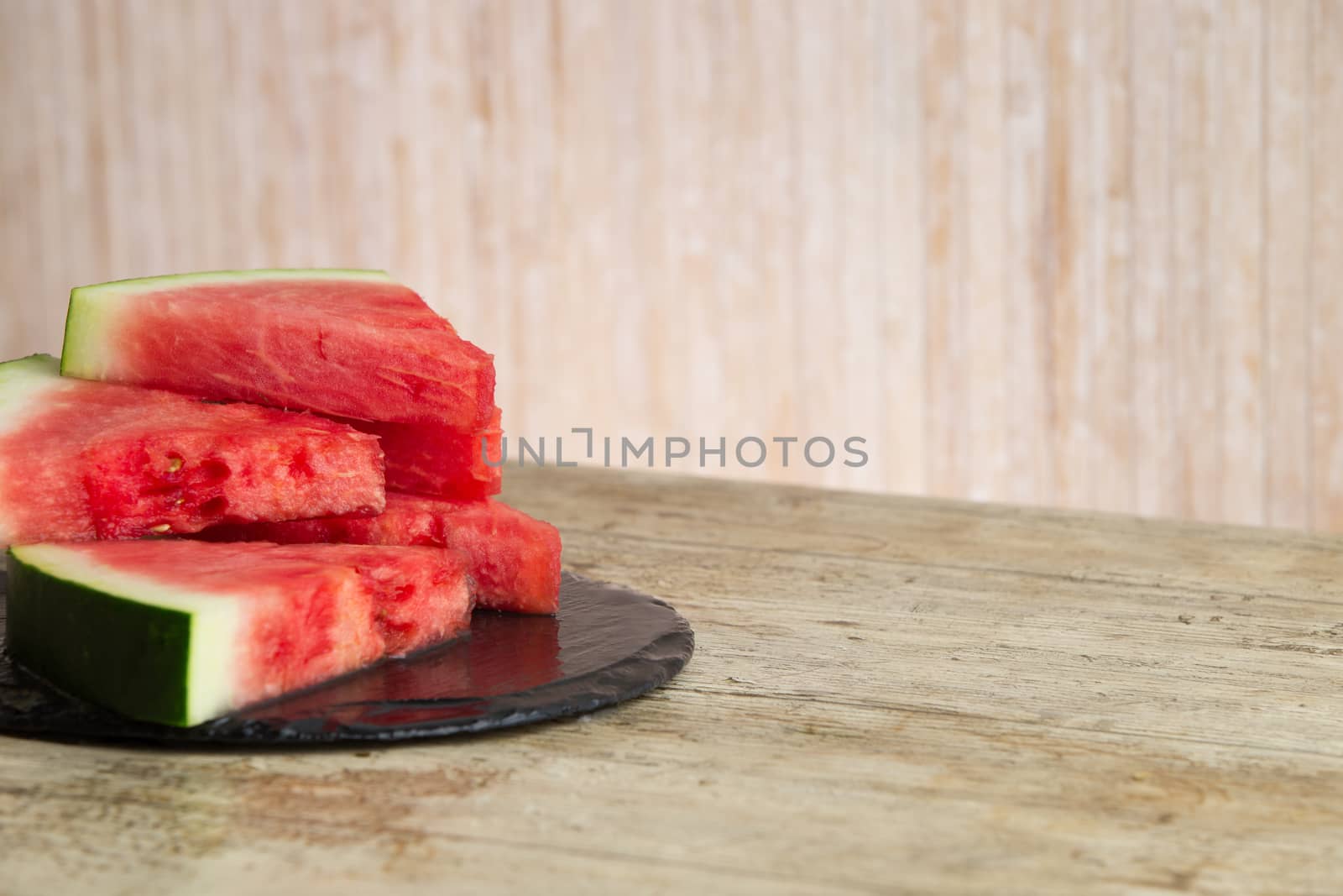 Triangular slices of watermelon overlaid on a black plate of wet slate in selective focus for copy space