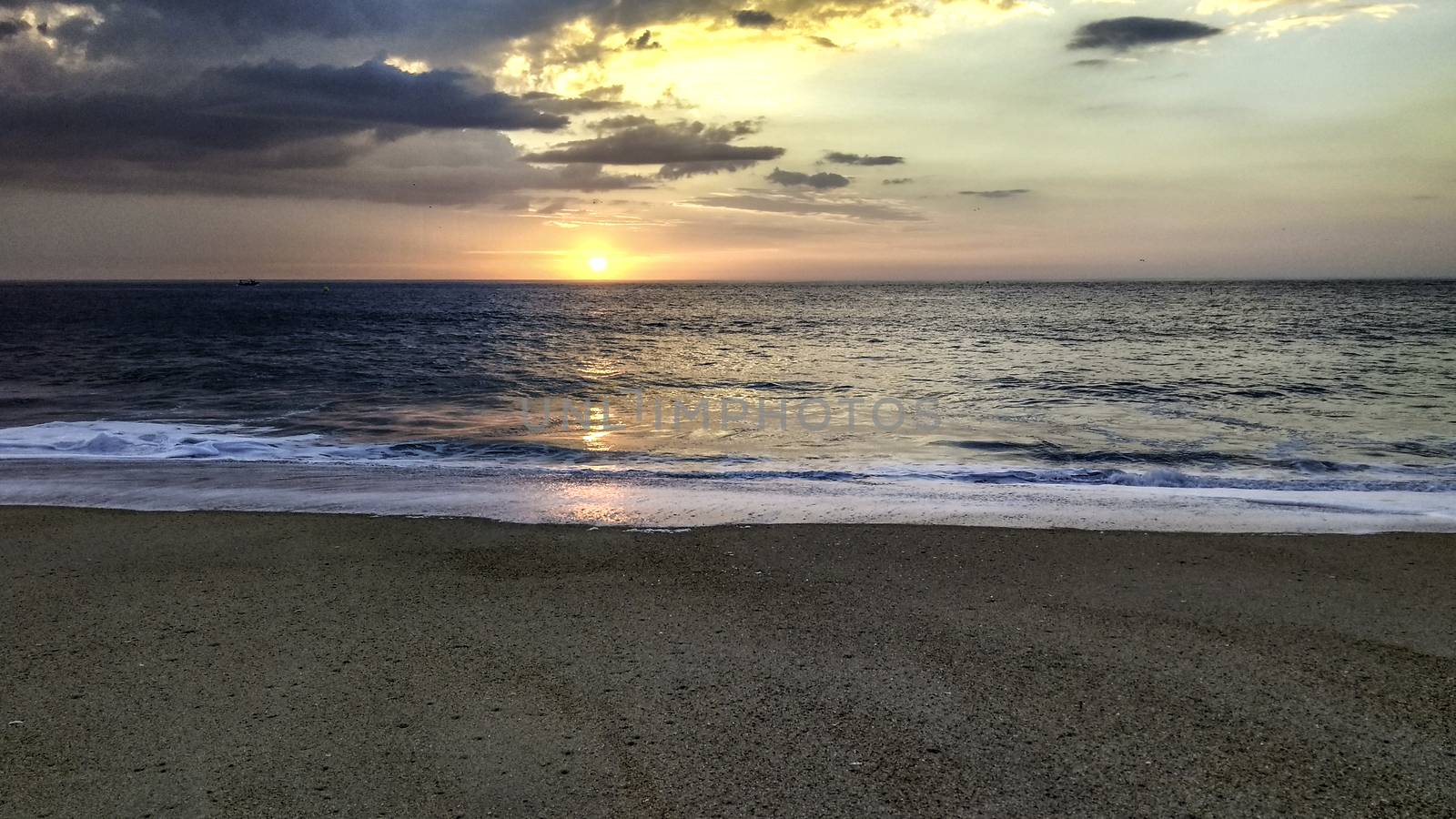 Sunset over the ocean from the shore of Nazaré beach, Playa do Norte, Portugal. The waves break on the shore reflecting the colors of the sky on the wet sand by robbyfontanesi