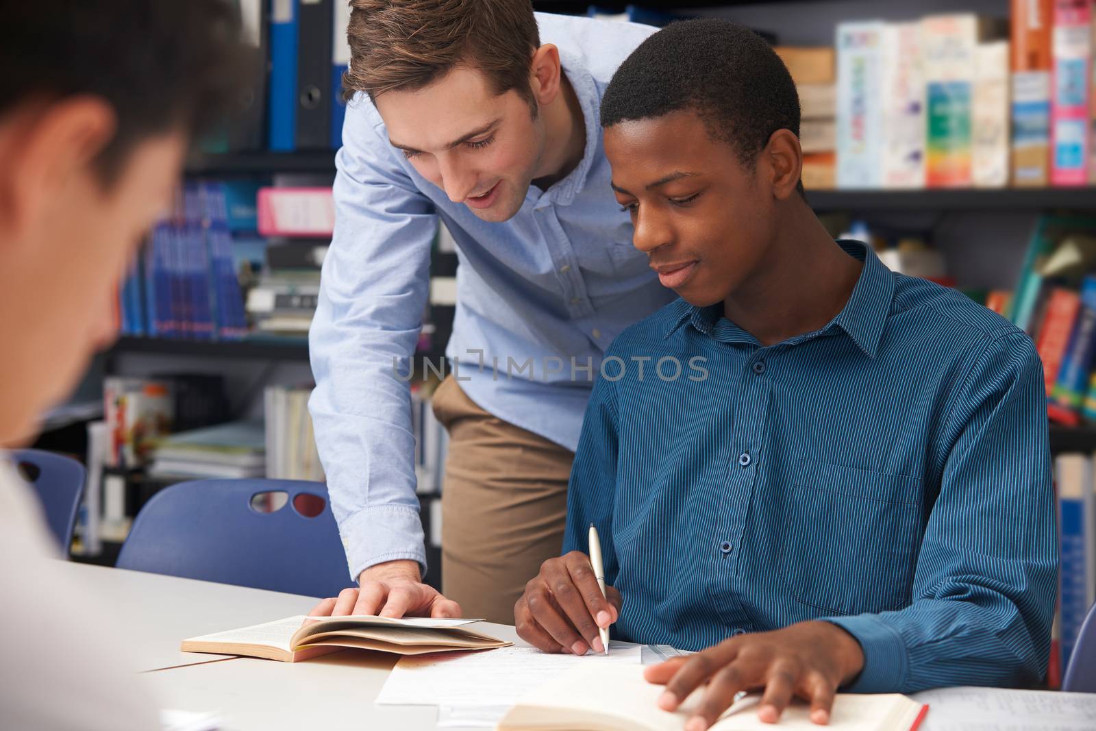 Teacher Helping Male Student In Classroom by HWS