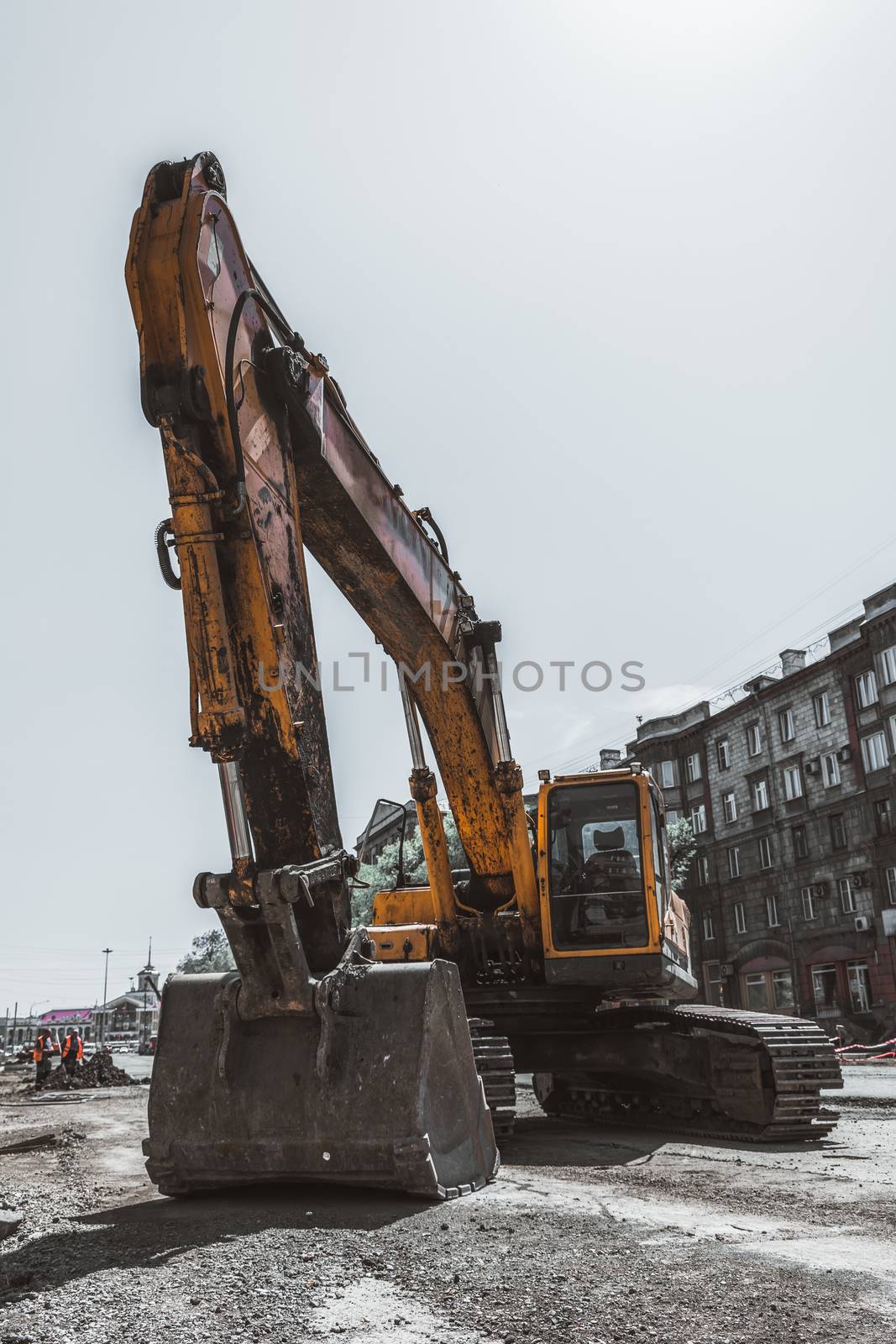 Excavator and his big bucket during the construction of the road against the backdrop of urban buildings