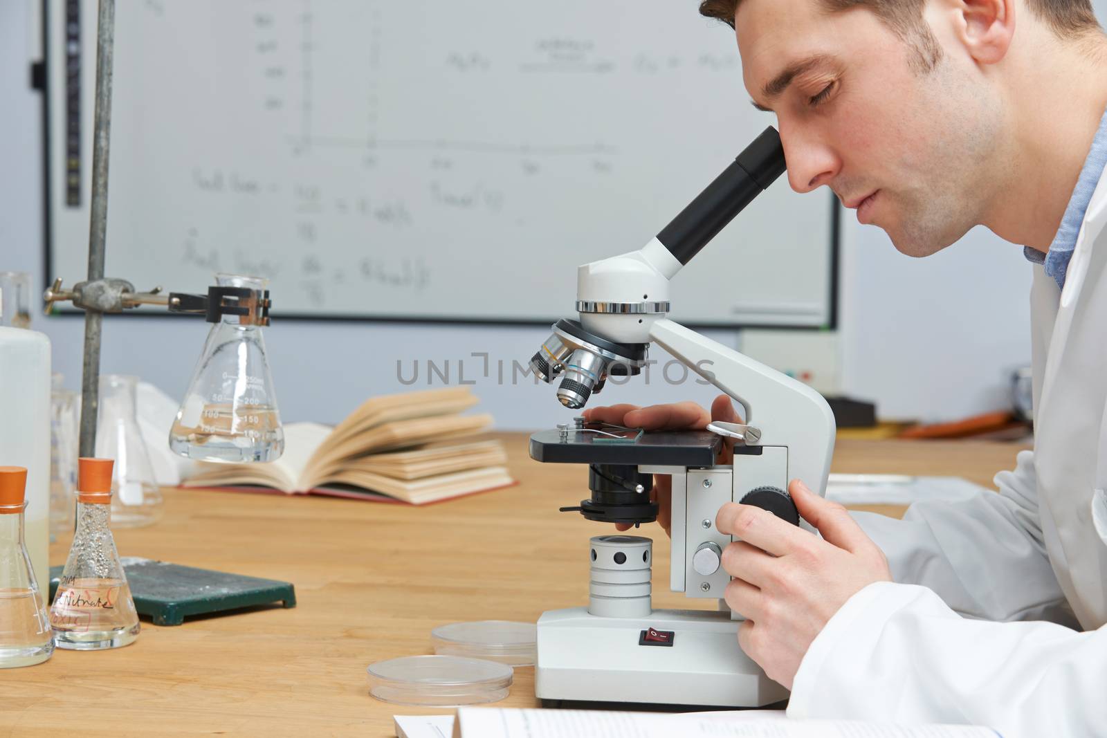 Male Biology Teacher Looking Through Microscope In Classroom