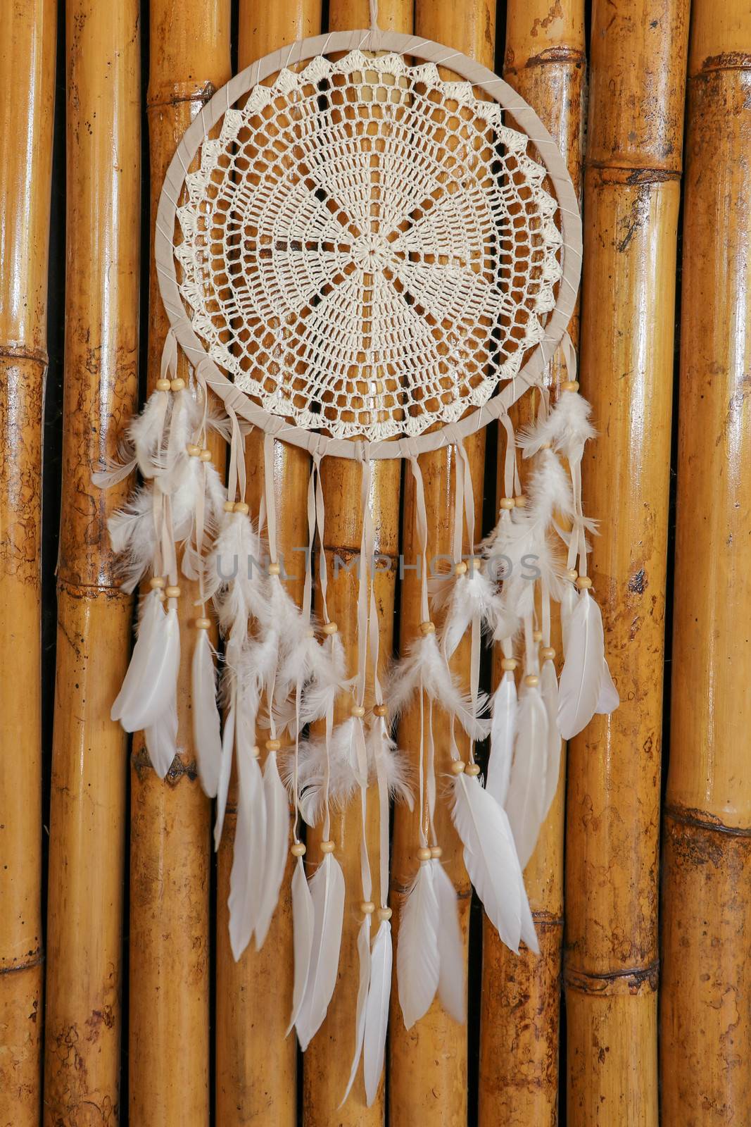 Dream catcher, decorated with white feathers and wooden beads, on a wooden surface. Dream catcher with wooden circle. Knitted Native American amulet with the symbol of Yin Yang on a wodden background.