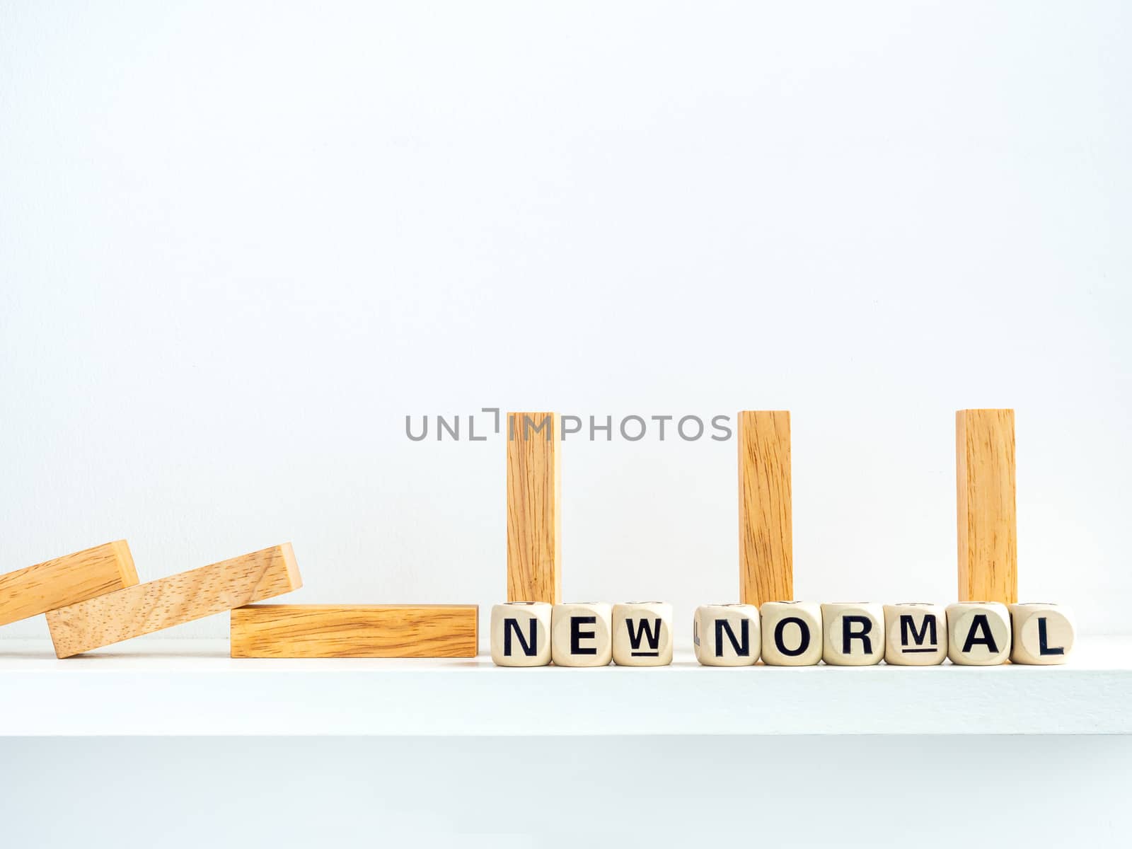 Social Distancing concept. Row of falling and standing wooden dominoes with distance space and New Normal, words on wooden alphabet cube on white background.