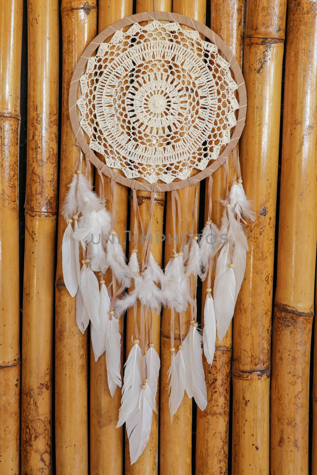 Dream catcher, decorated with white feathers and wooden beads, on a wooden surface. Dream catcher with wooden circle. Knitted Native American amulet with the symbol of Yin Yang on a wodden background.