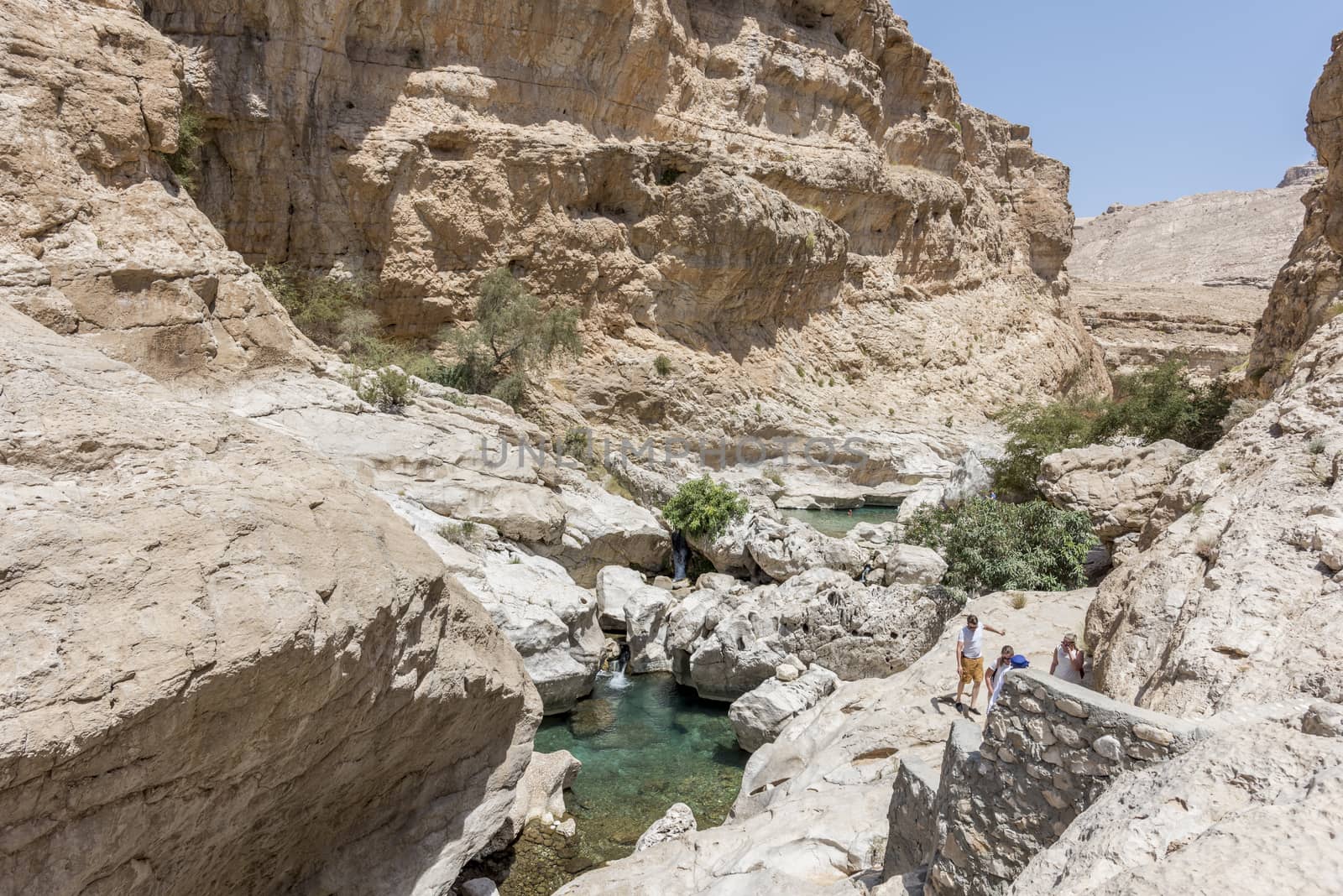Tourists and guide trekking near the river and pool in the canyon of Wadi Bani Khalid,  in Oman