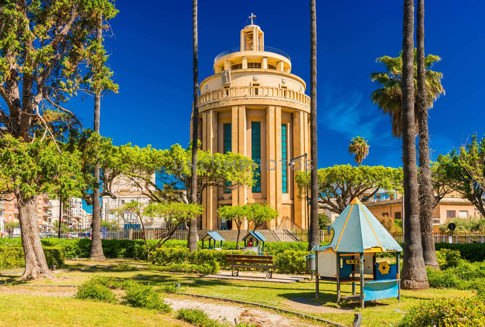 Syracuse - April 2019, Italy: Church of Saint Thomas "al Pantheon" (Chiesa di San Tommaso) viewed through palm trees and a playground in the Park of the Syracusan Forum (Parco del Foro Siracusano)