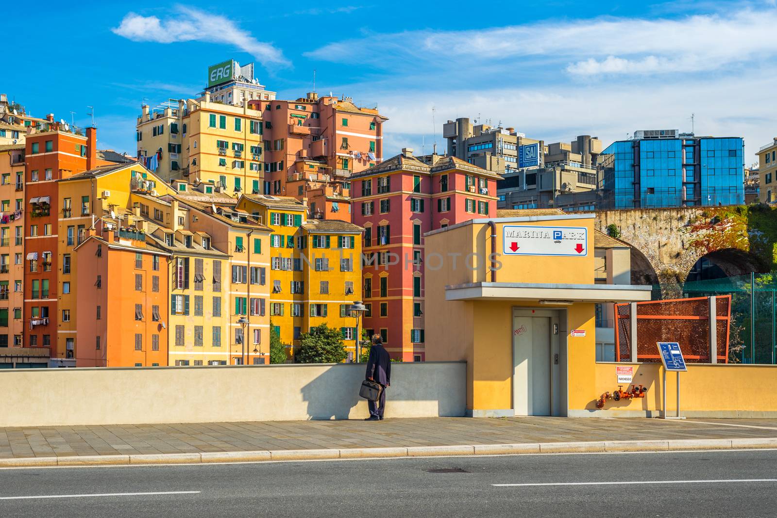 Genoa (Genova) - November 2013, Liguria, Italy: Man in black suit with case stands near to the parking entrance and colored houses on the background