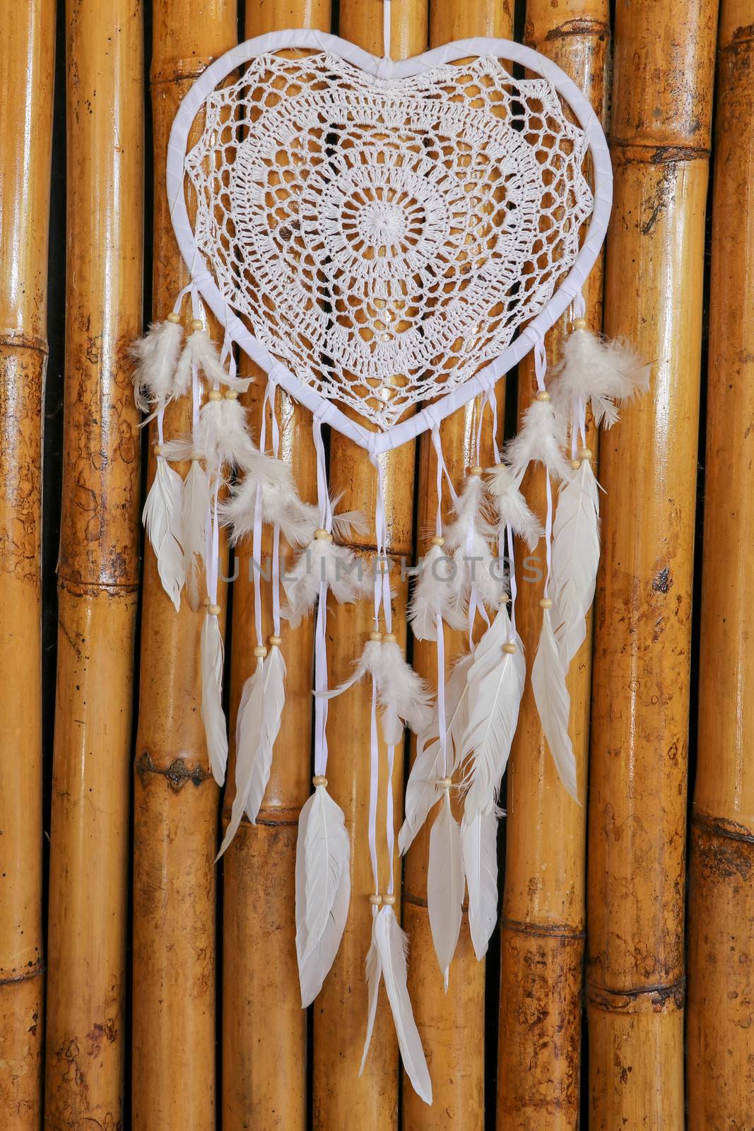 Dream catcher shaped heart with beige peacock feathers on the bamboo wall.