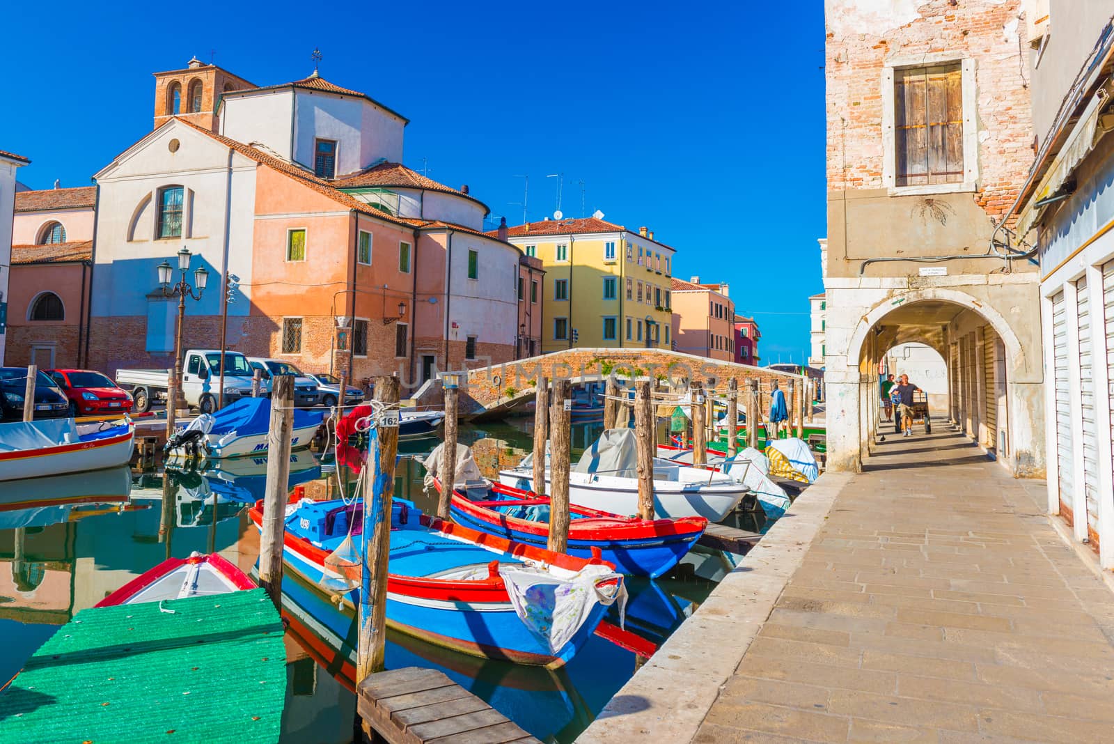 Chioggia - September 2016, Italy: Street of Chioggia, the town also known as a part of Venice. Boats lying on water in central canal "Vena". Old historical buildings and church against the blue sky