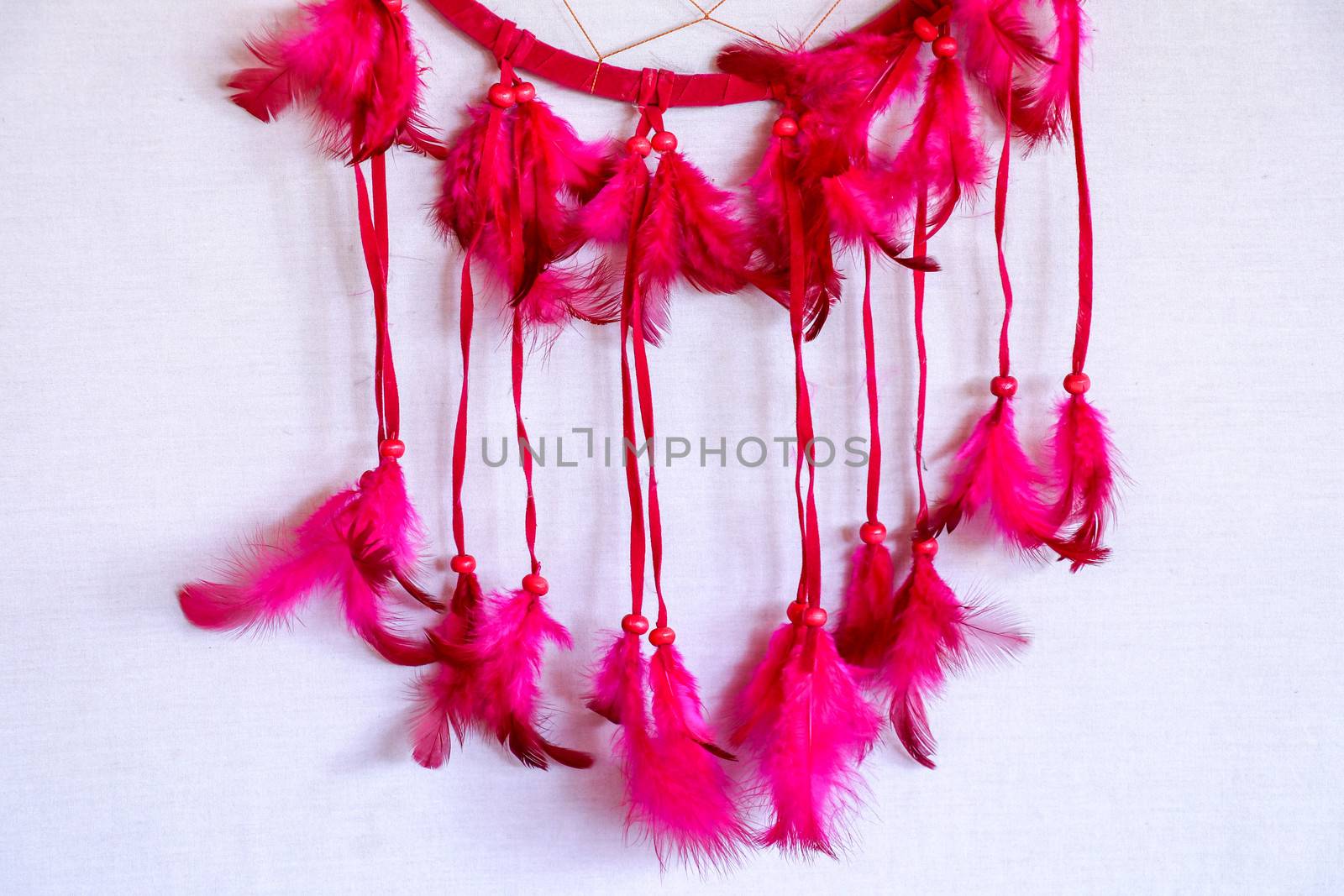 Closeup of beautiful colorful decorative red and blue feathers as dream catchers hanging near bright beads white pink and yellow colors on exhibition outdoor on blurred background, horizontal picture.
