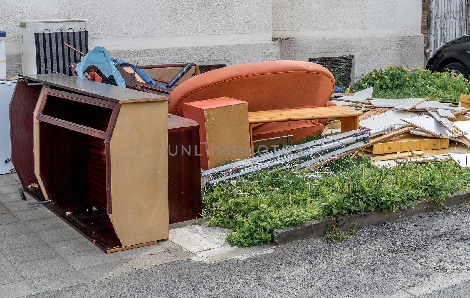 Bulky waste with cupboards, a sofa and furniture on the lawn in front of an apartment building by geogif